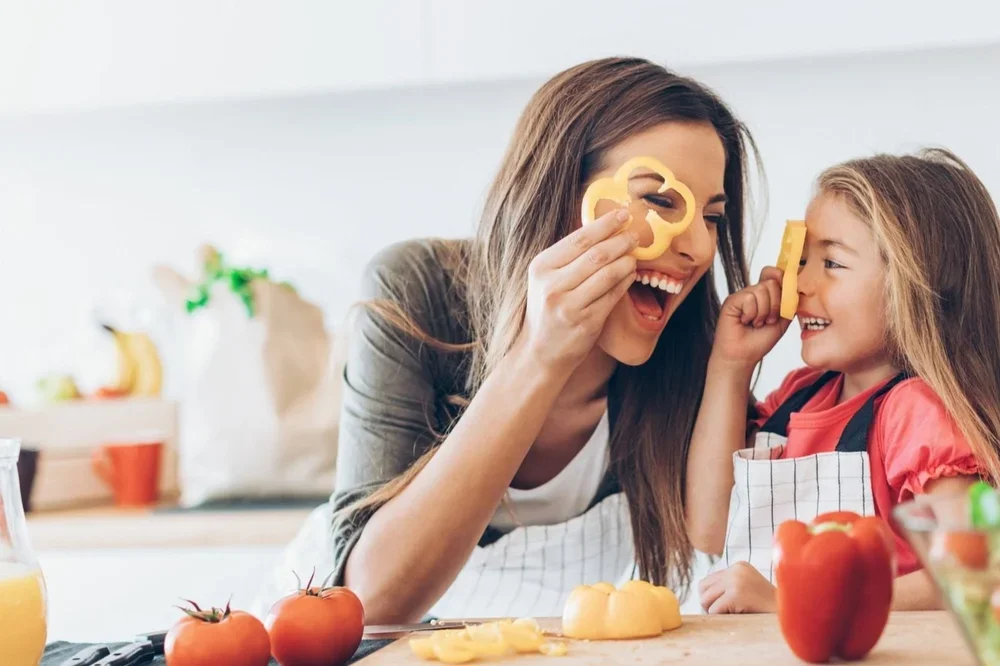 a mom and daughter cooking in a kitchen, and goofing off with pepper slices on their eyes