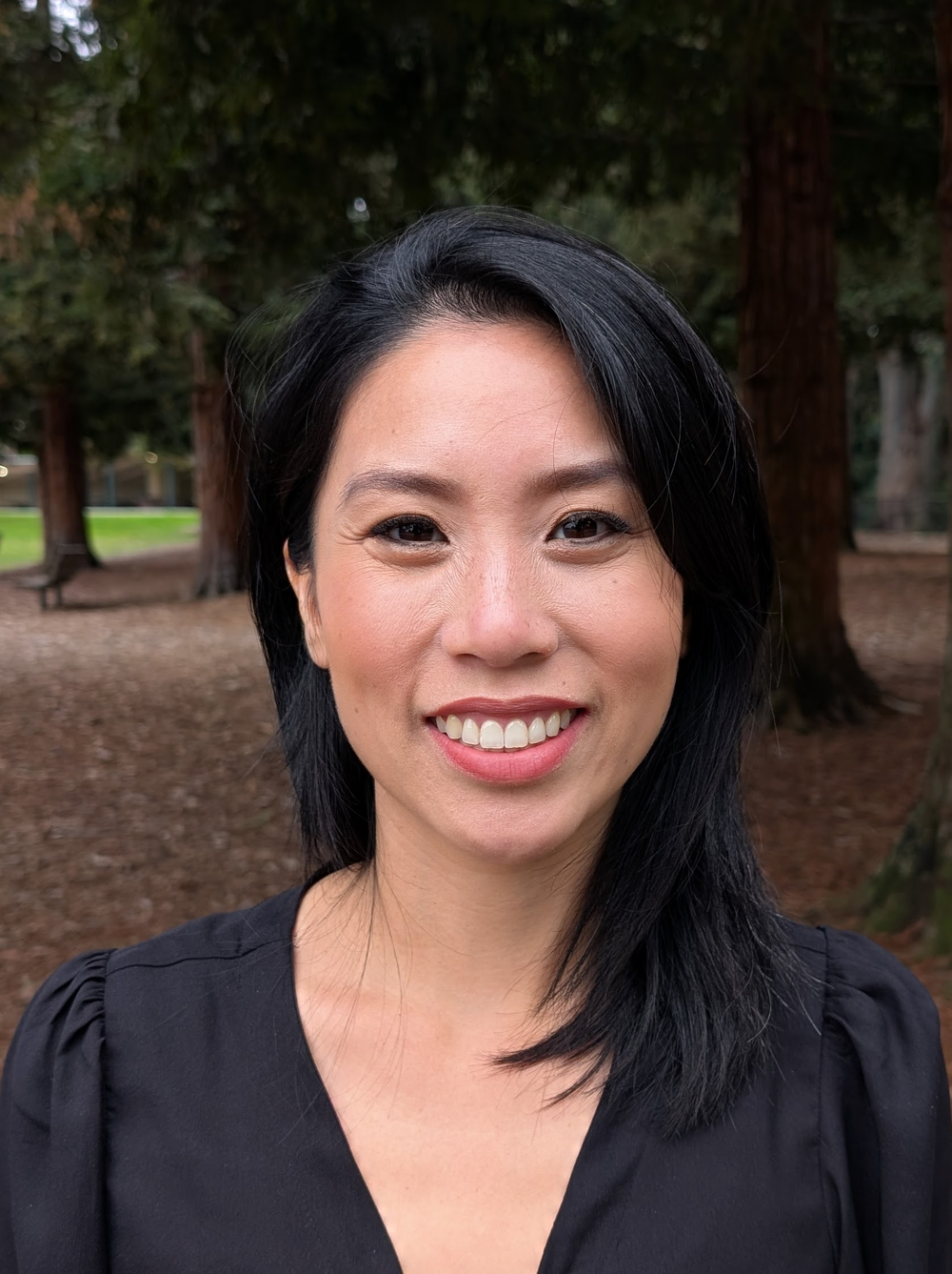 headshot of Serena Cheng, a woman of asian descent, smiling and wearing a black v-neck shirt against a natural background