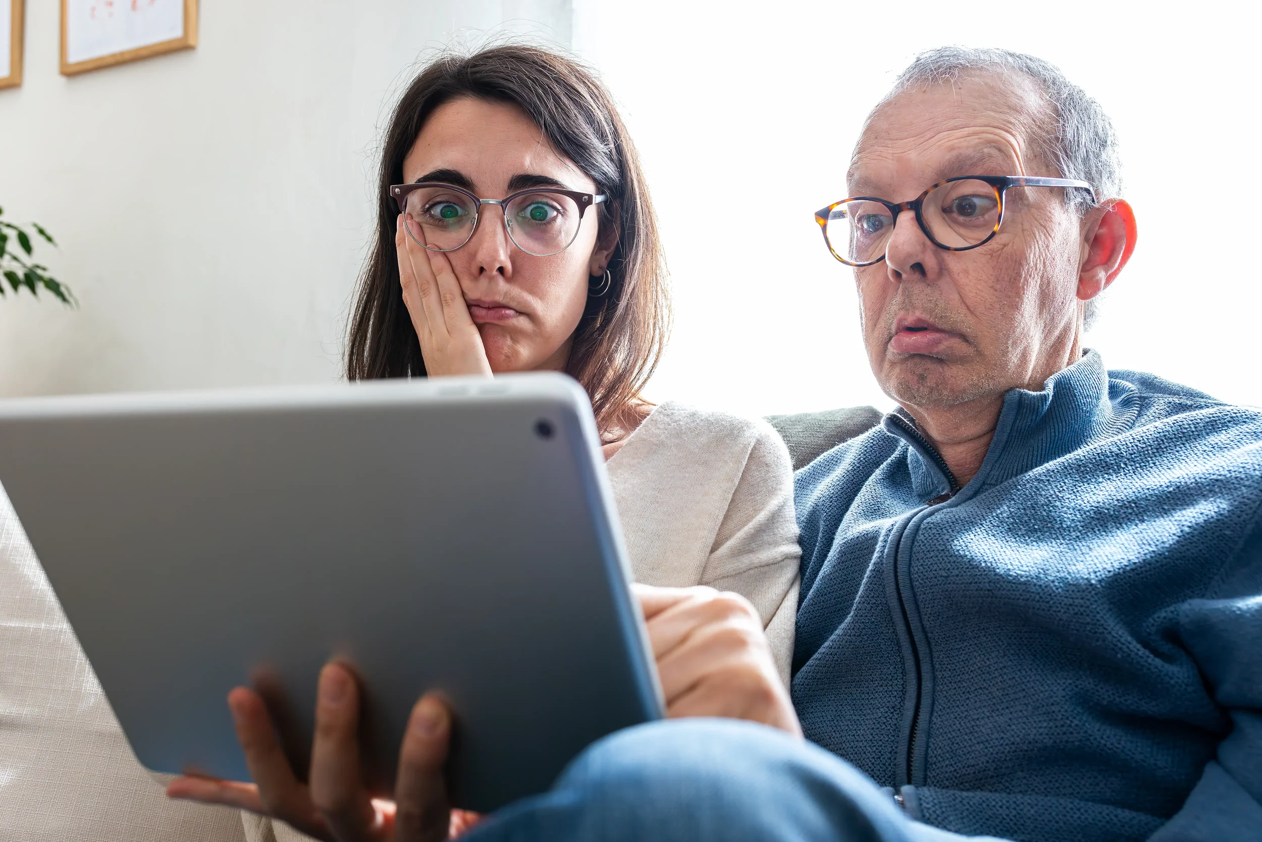 Father and adult daughter looking confused while reviewing aged care options and costs on a laptop at home.