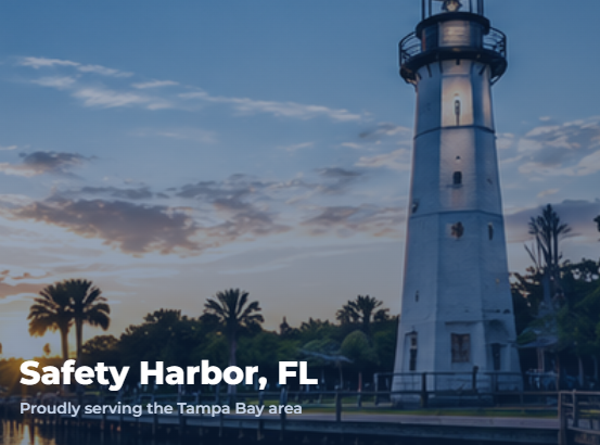 A white lighthouse on the shoreline at sunset with palm trees and a partly cloudy sky in the background.
