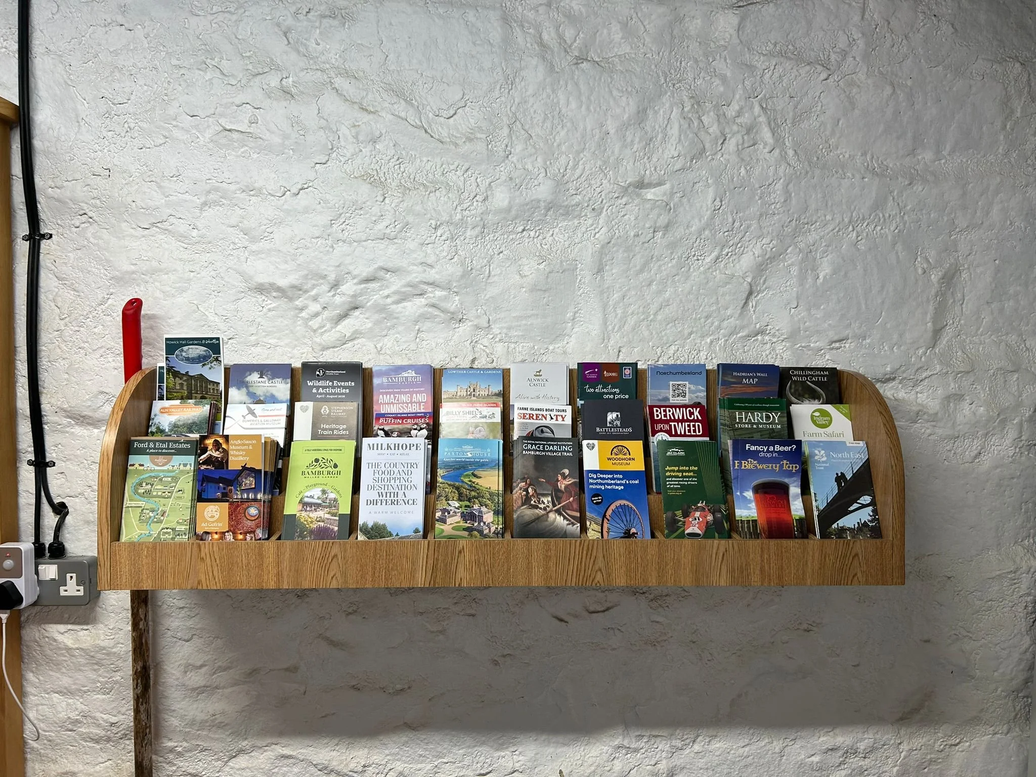 Display rack with travel brochures and maps against a textured white wall.