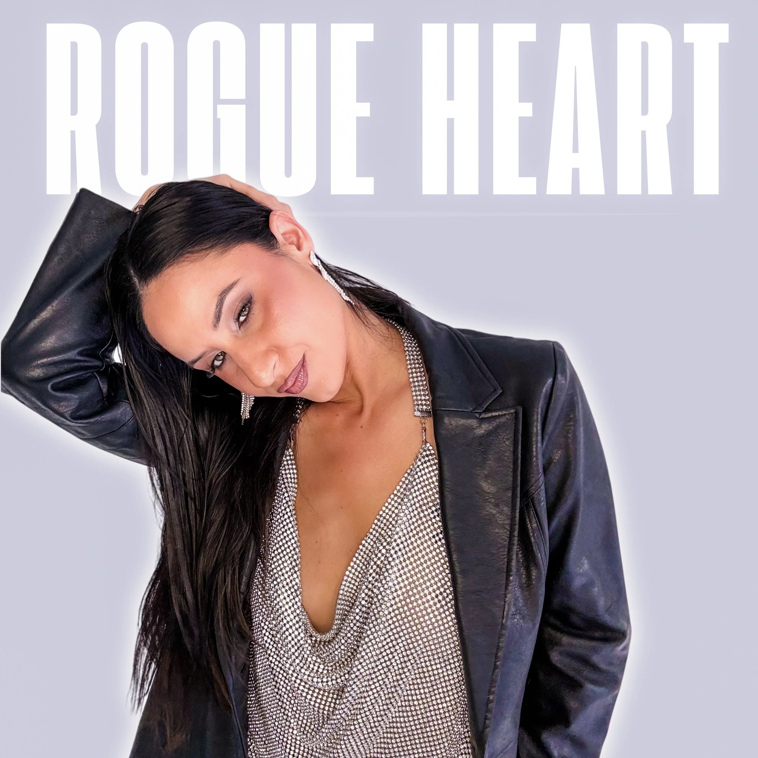 Close-up of a woman with long dark hair lying on a black leather chair, wearing a black leather jacket and a stylish silver necklace. Behind her, in large white text on a light gray background, the words 'ROGUE HEART" are partially visible.