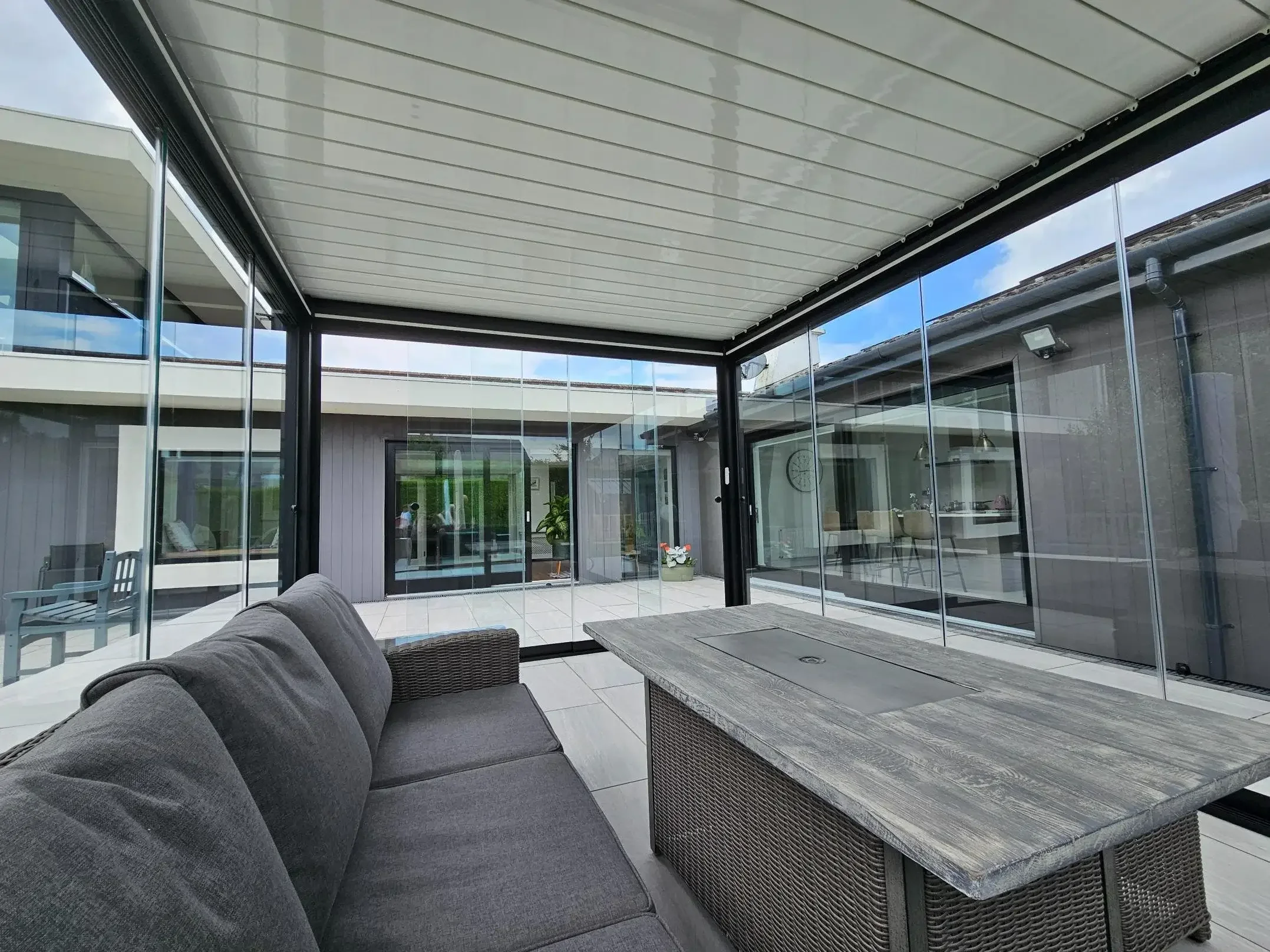 View of a covered outdoor patio area with glass walls, outdoor furniture, and a dining table.