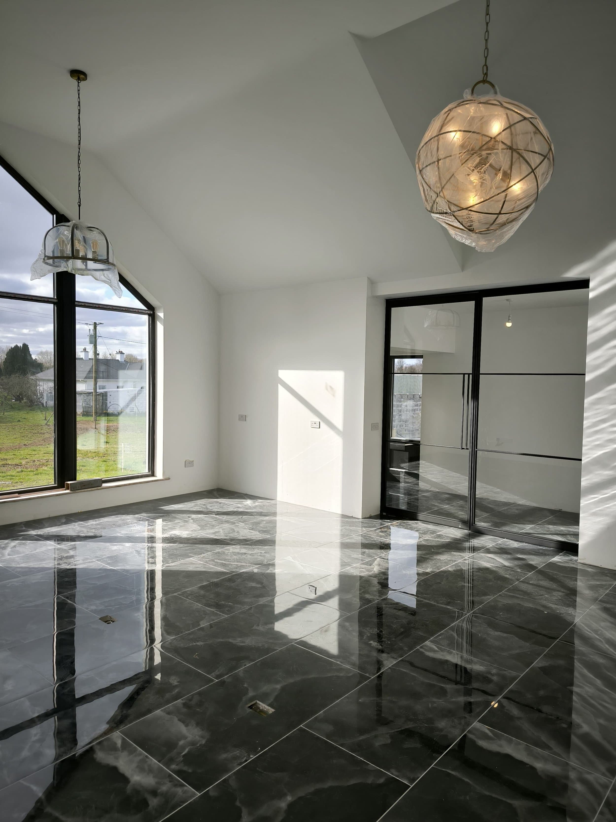 Bright, modern room with large windows, glass doors, shiny black marble floor, and two hanging pendant lights.