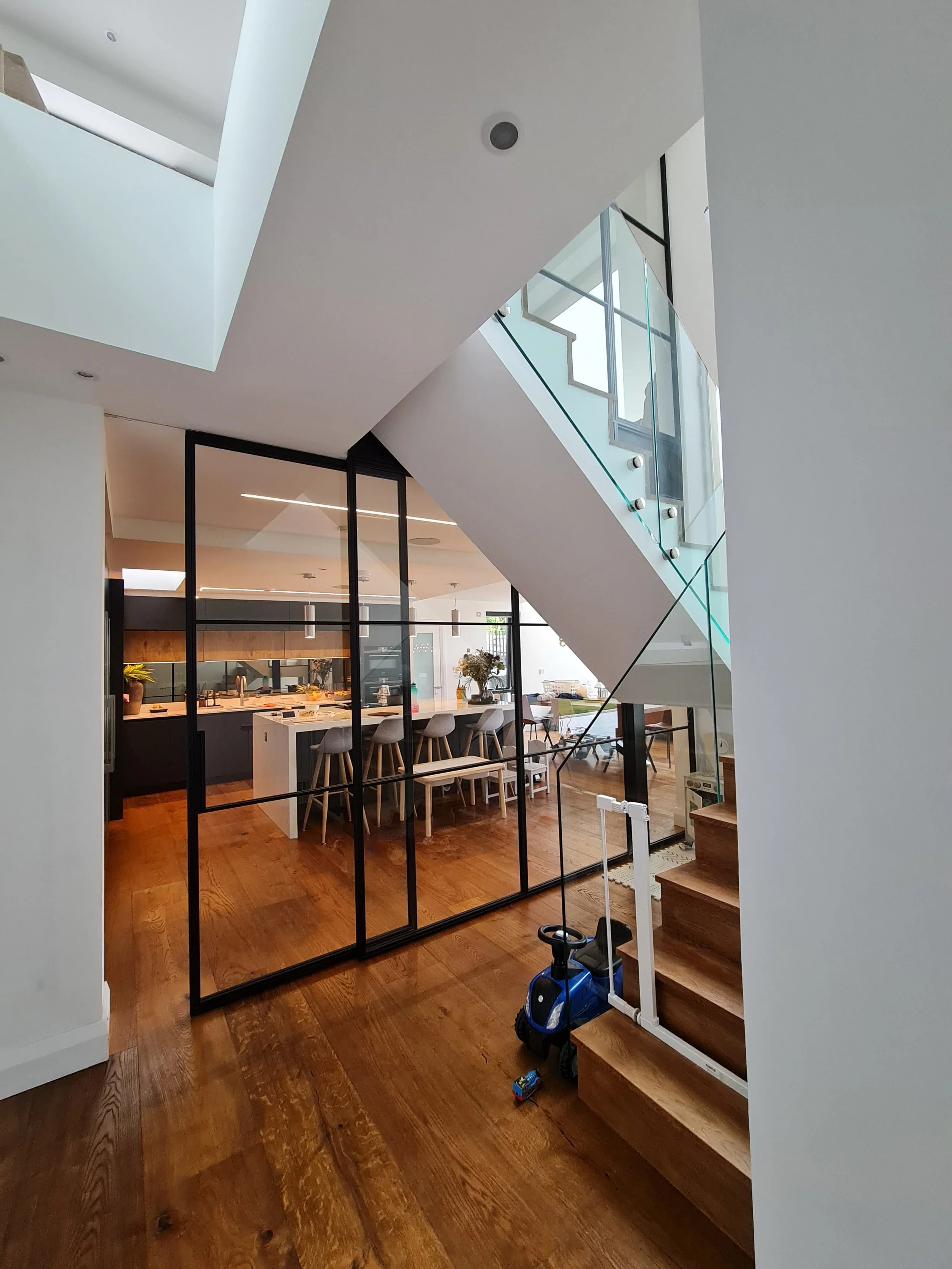 View into kitchen with sliding steel glass door and two story steel glass partition and stairs with frame-less glass side