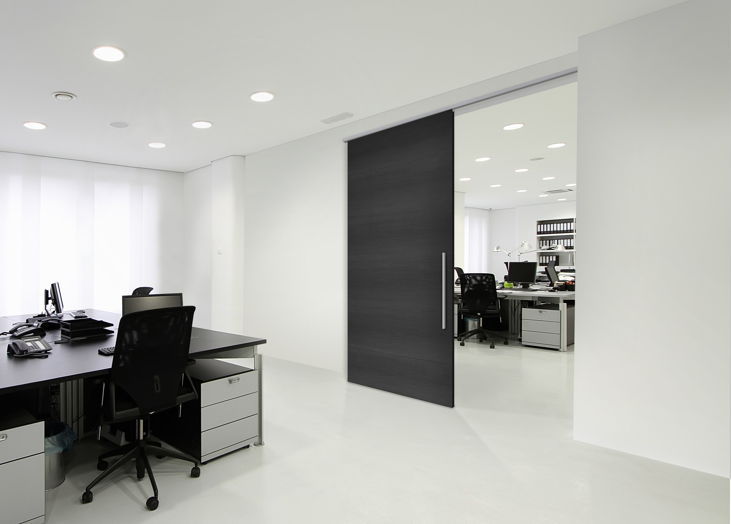 Modern office with sliding wooden door on a Klein Lite 100 retract sliding system,  white walls, ceiling lights, black desks, and chairs