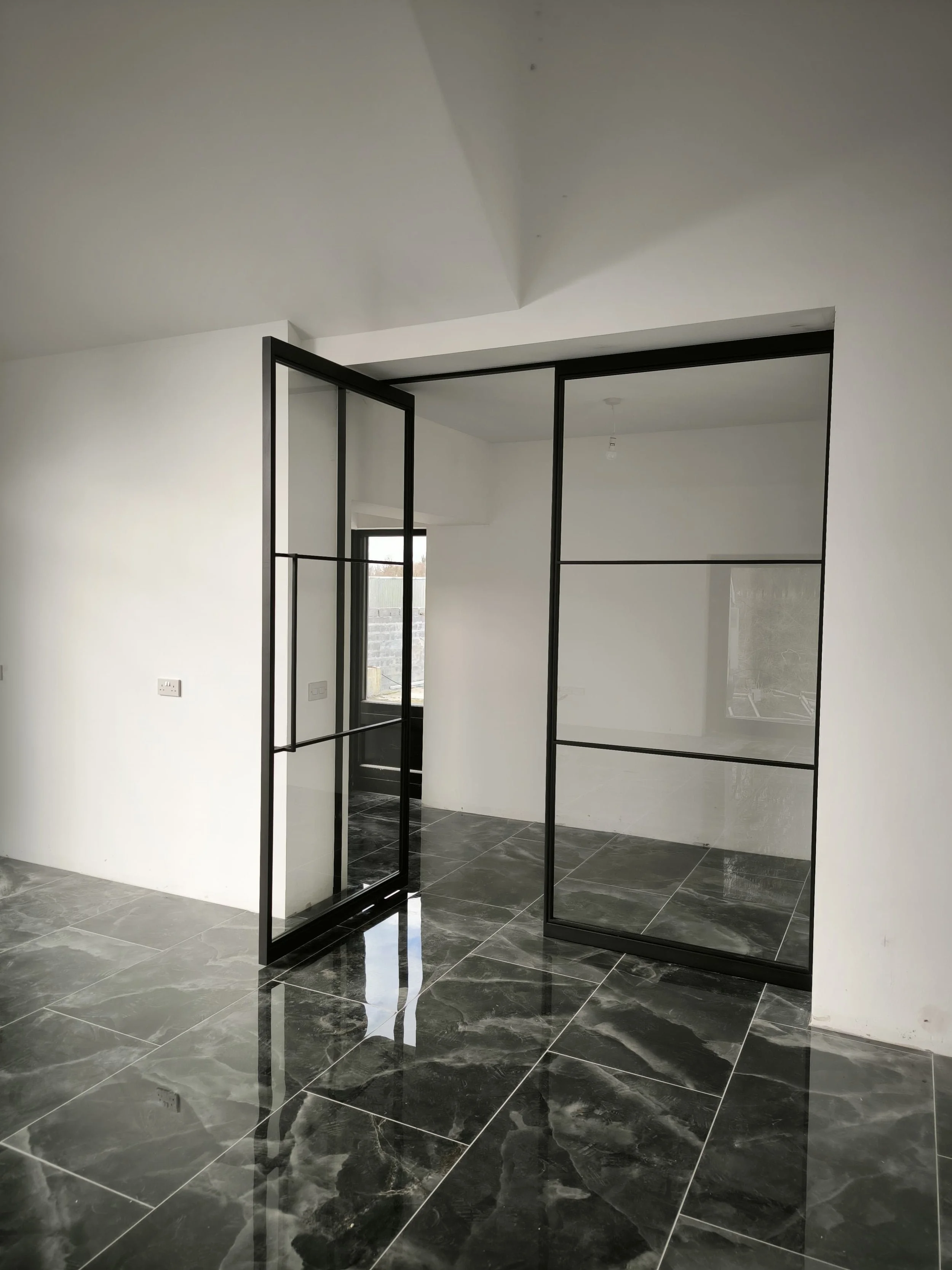 Modern room with black-framed glass double doors and shiny black marble floor tiles, white walls, and minimal decor.