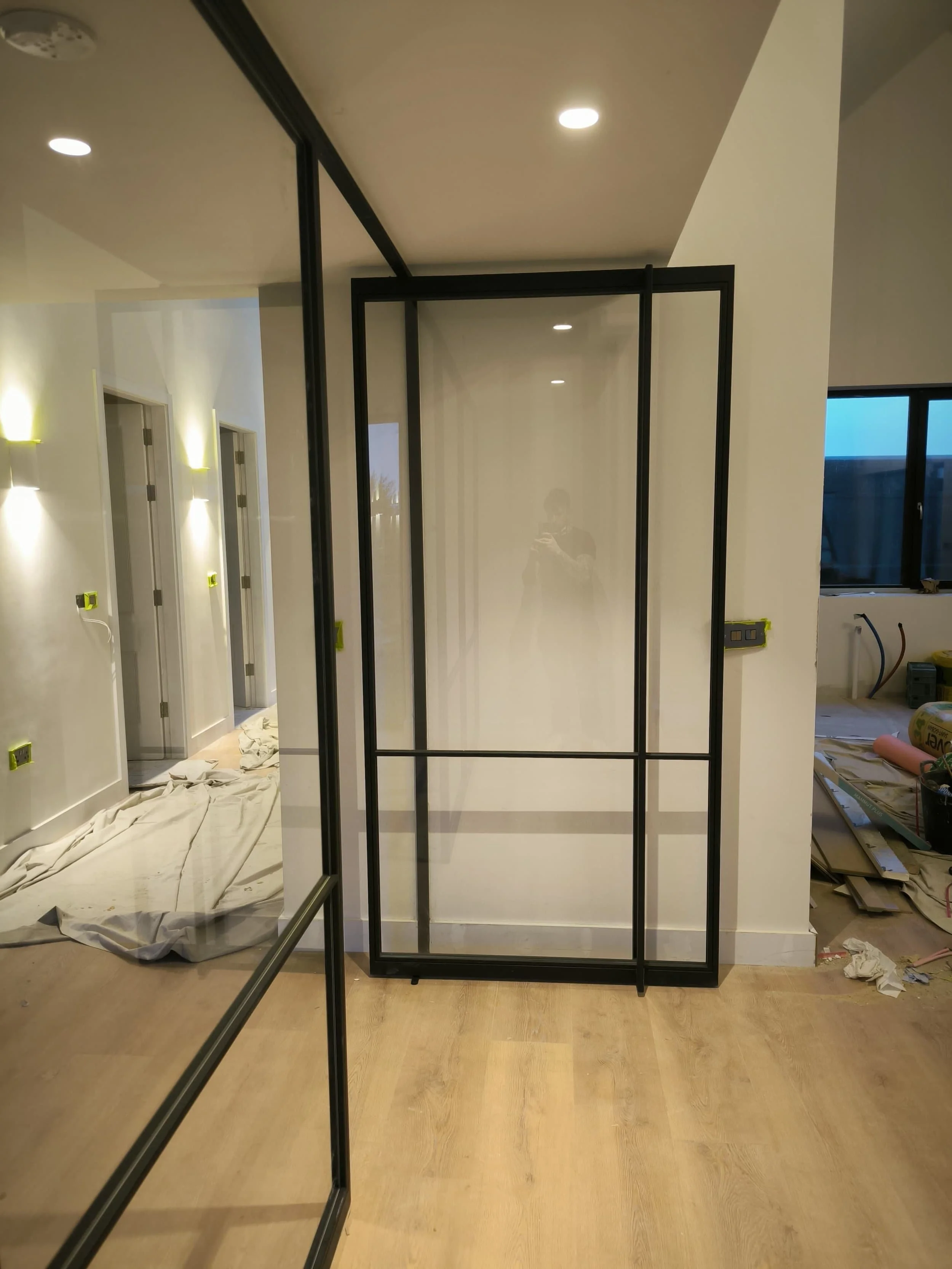 A modern interior hallway under renovation, with glass doors, wooden floors, and tools and covers scattered on the floor.