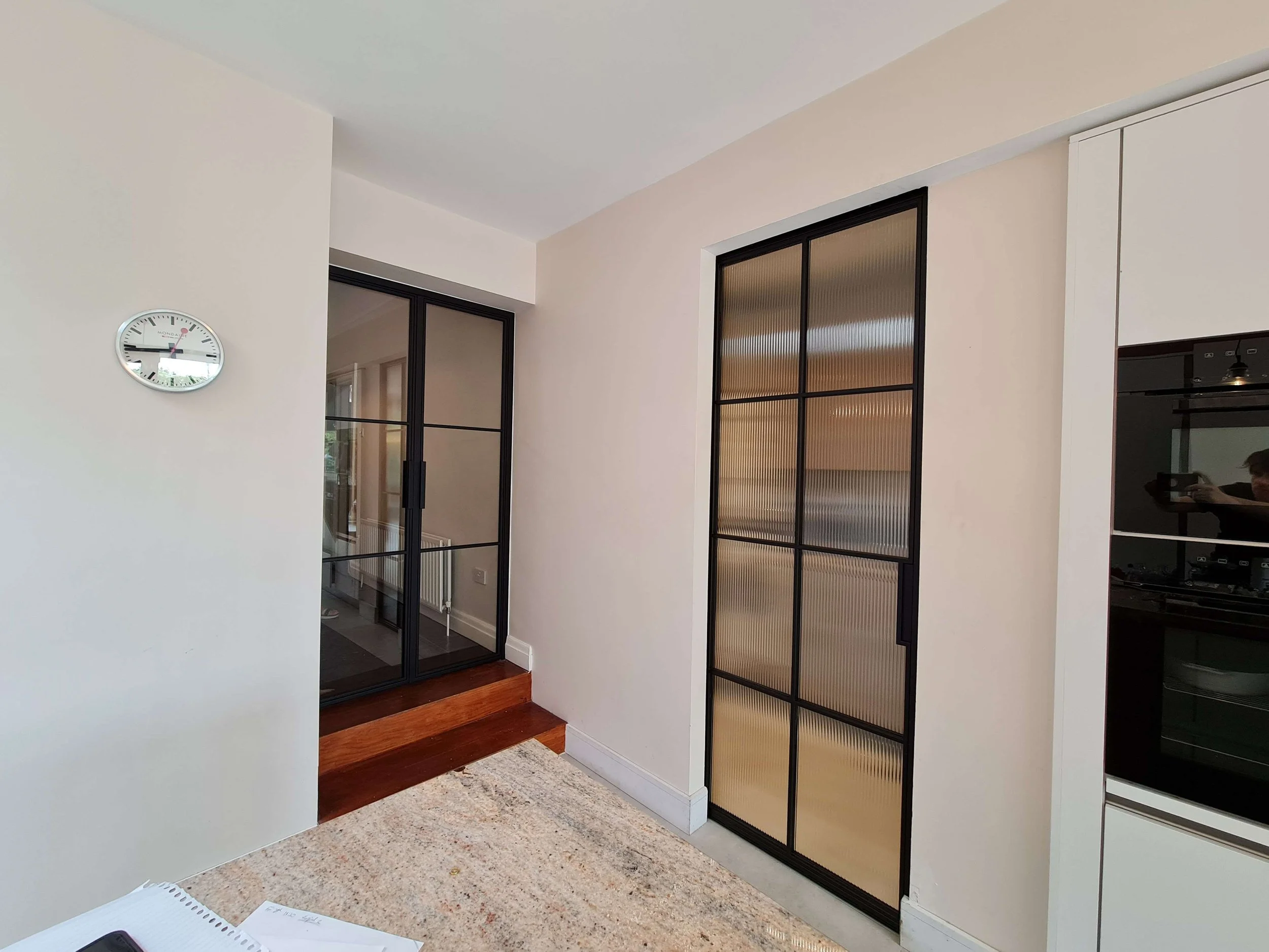 Corner of kitchen with steps up to black steel double hinged doors and pocket door with fluted glass separating pantry and kitchen