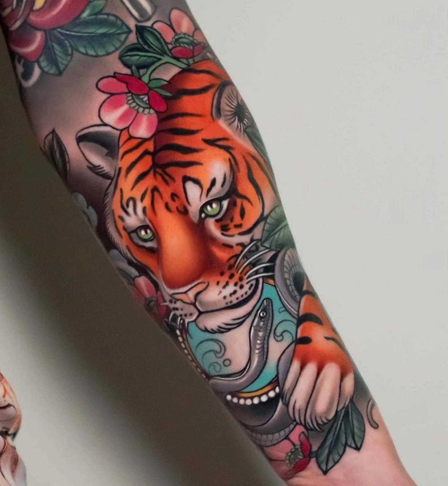 Tattoo of a tiger with green eyes surrounded by roses and leaves.