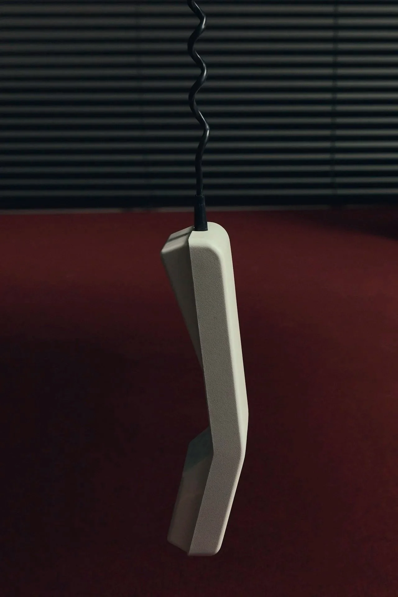 A white telephone with a curved handle hanging on a black wire hook, with a black and gray striped background and a red surface below.