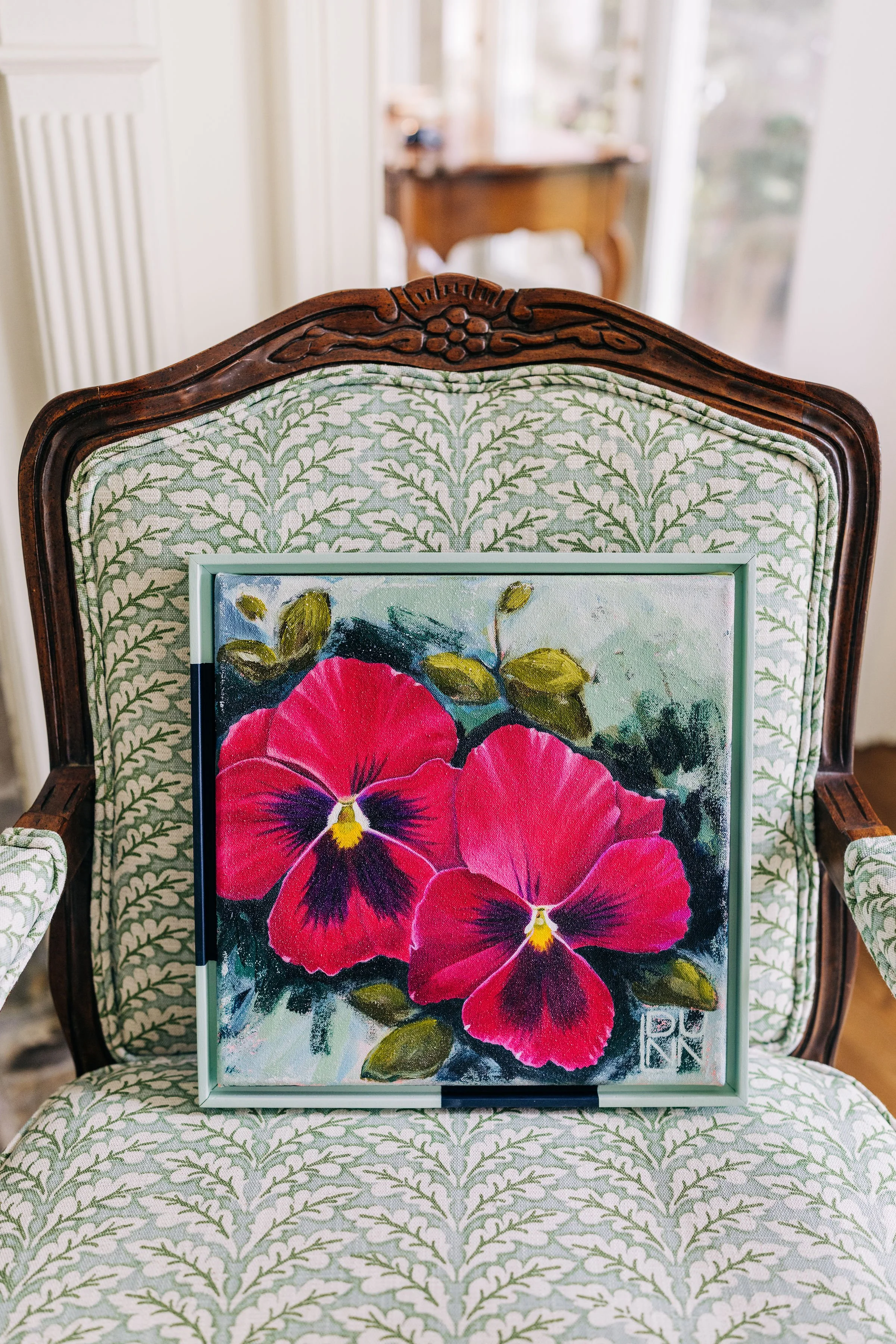 Painting of two red and purple pansy flowers with green leaves, resting on a patterned cushion. Painting by Laura Dunn available with the Campbell Collective.