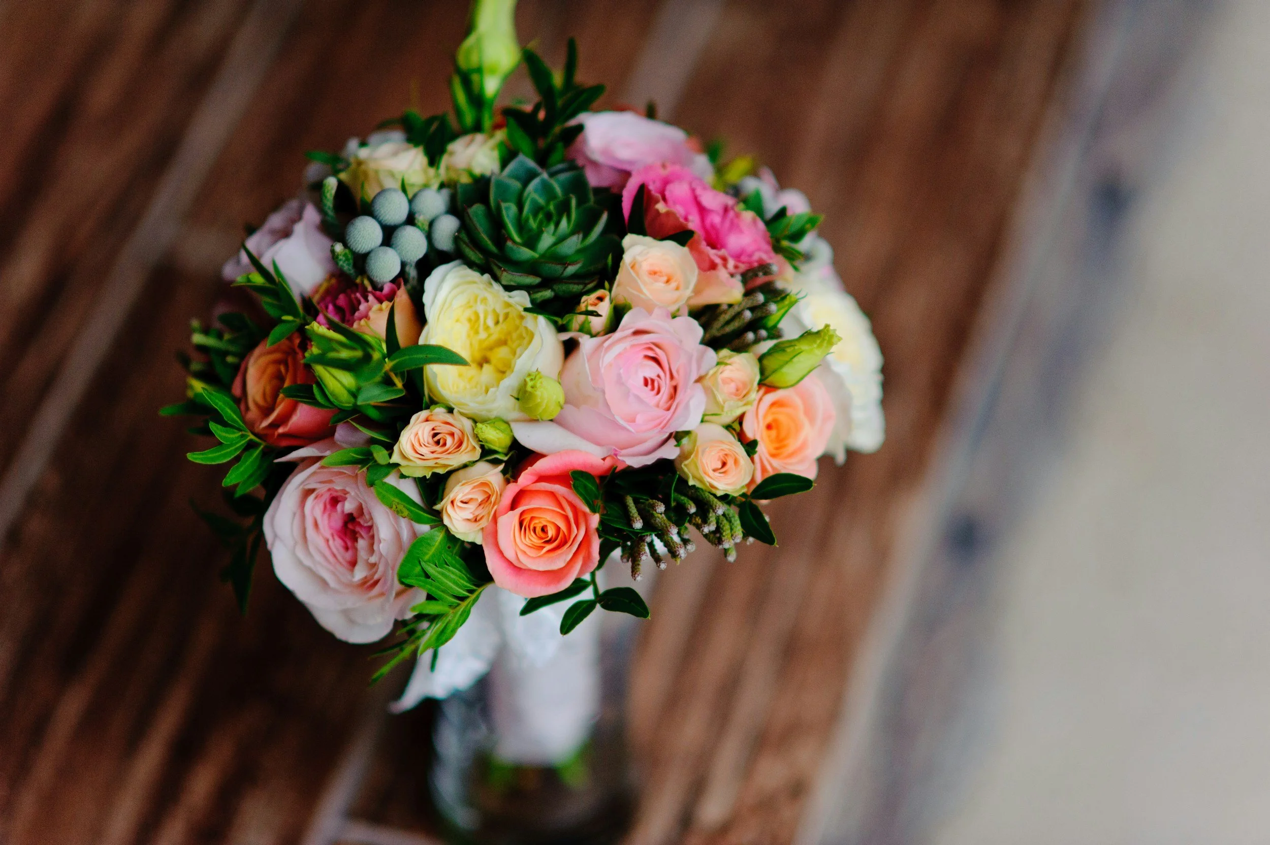 Colorful flower bouquet consisting of roses, succulents, and greenery on a wooden surface.