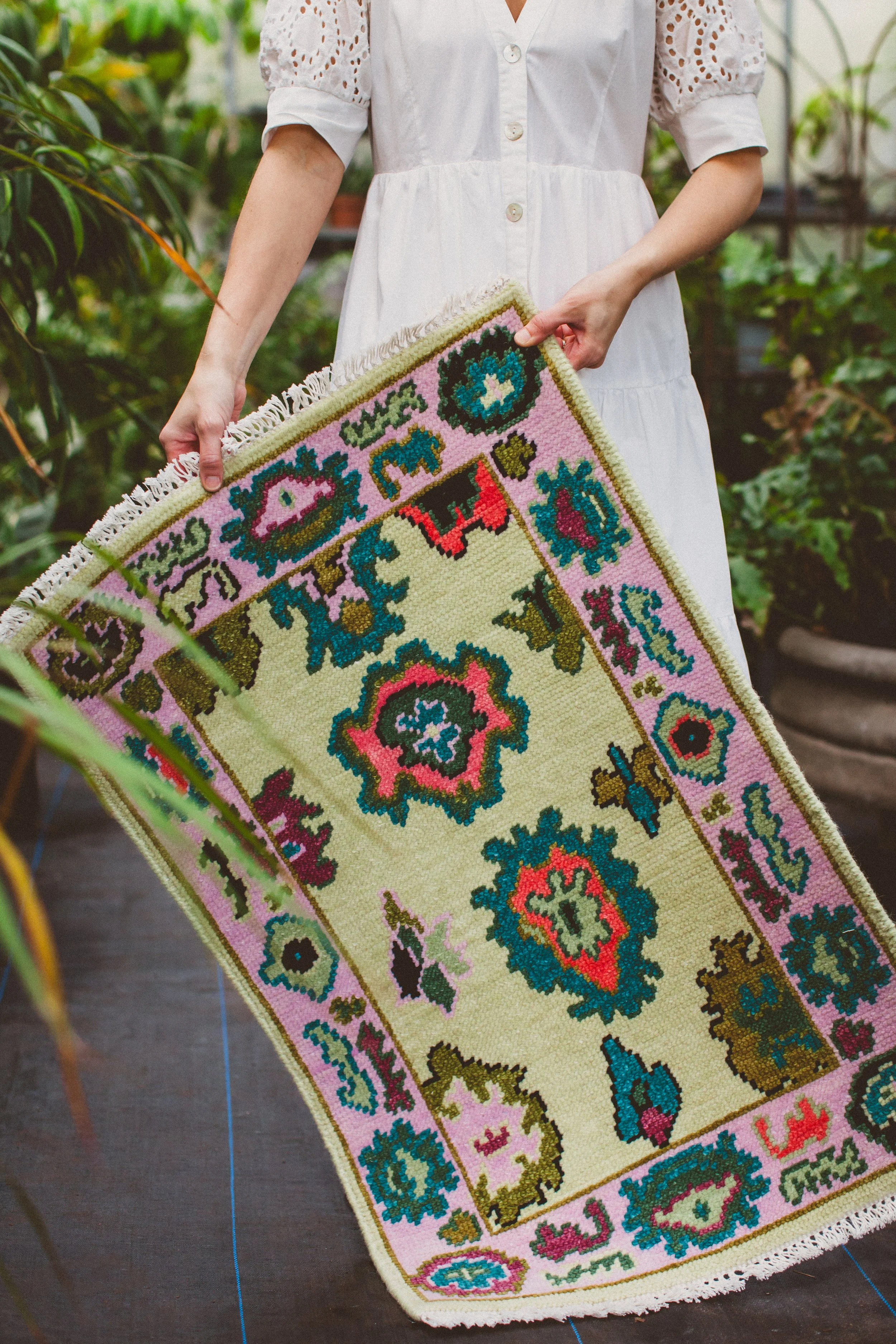 colorful oushak rug held by artist with plants