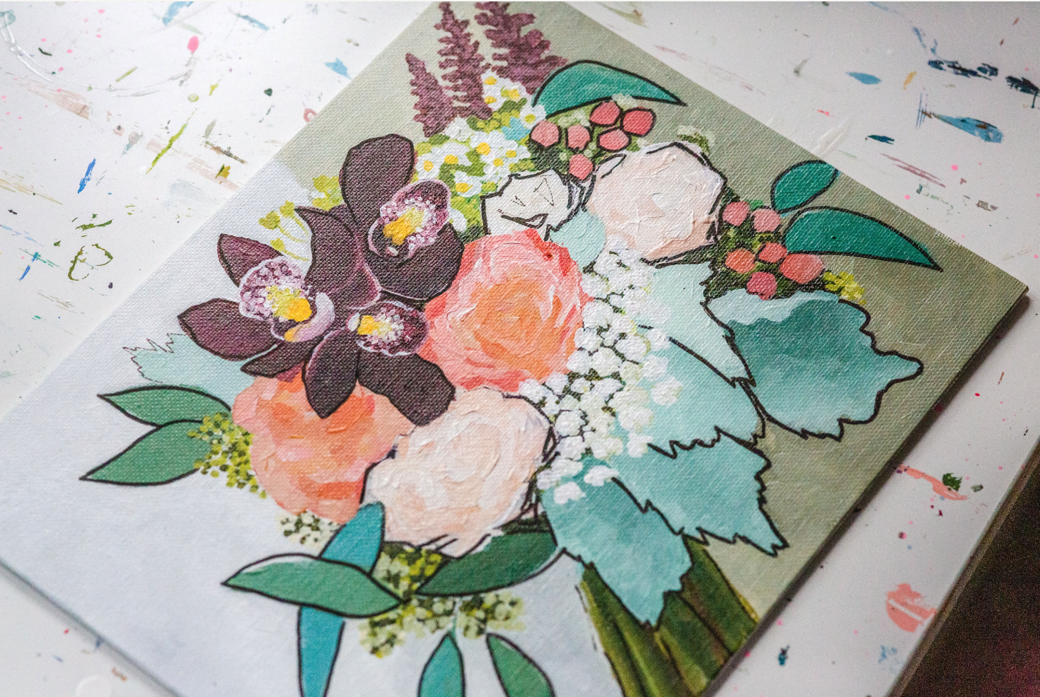 Watercolor painting of a floral bouquet with purple orchids, pink roses, white blooms, and green leaves on a canvas, placed on a paint-splattered surface.