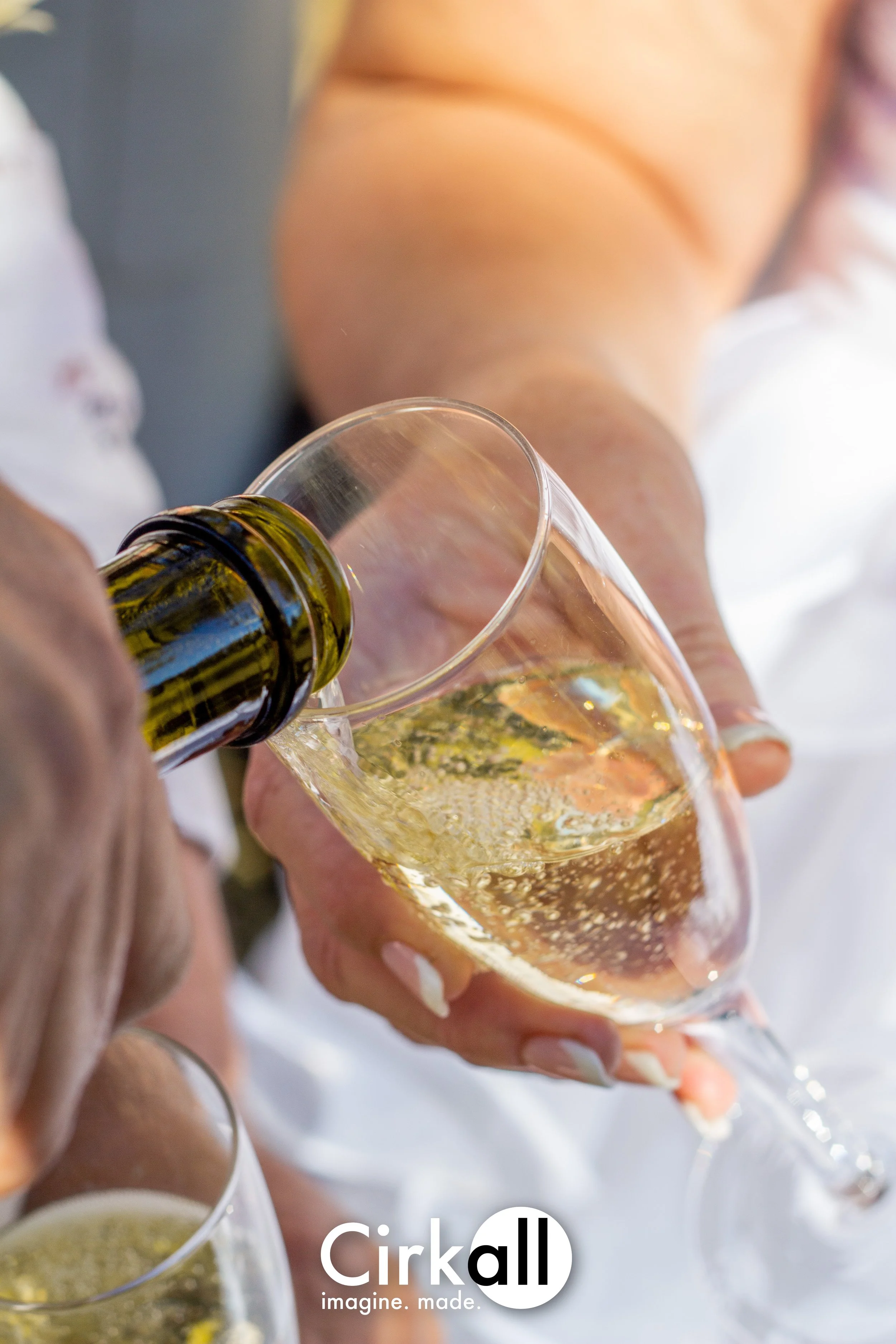 Person pouring sparkling wine into a wine glass at a celebration or gathering.