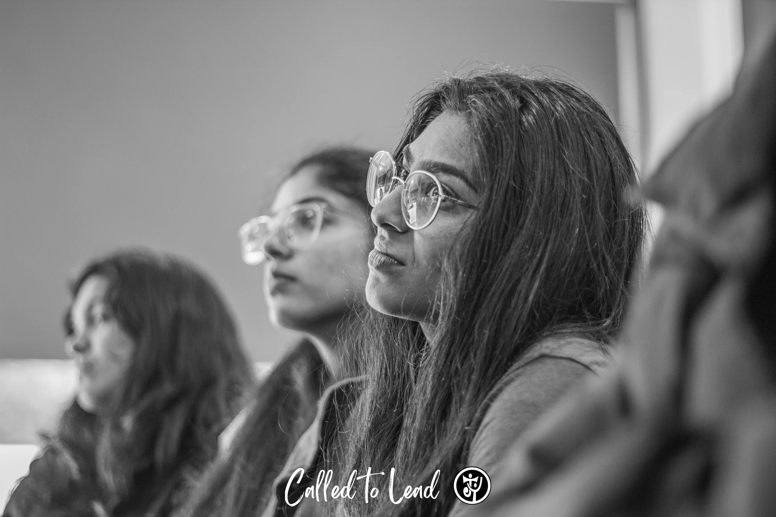 A group of women wearing glasses attentively listening during a meeting or seminar, with the focus on the woman in the center.