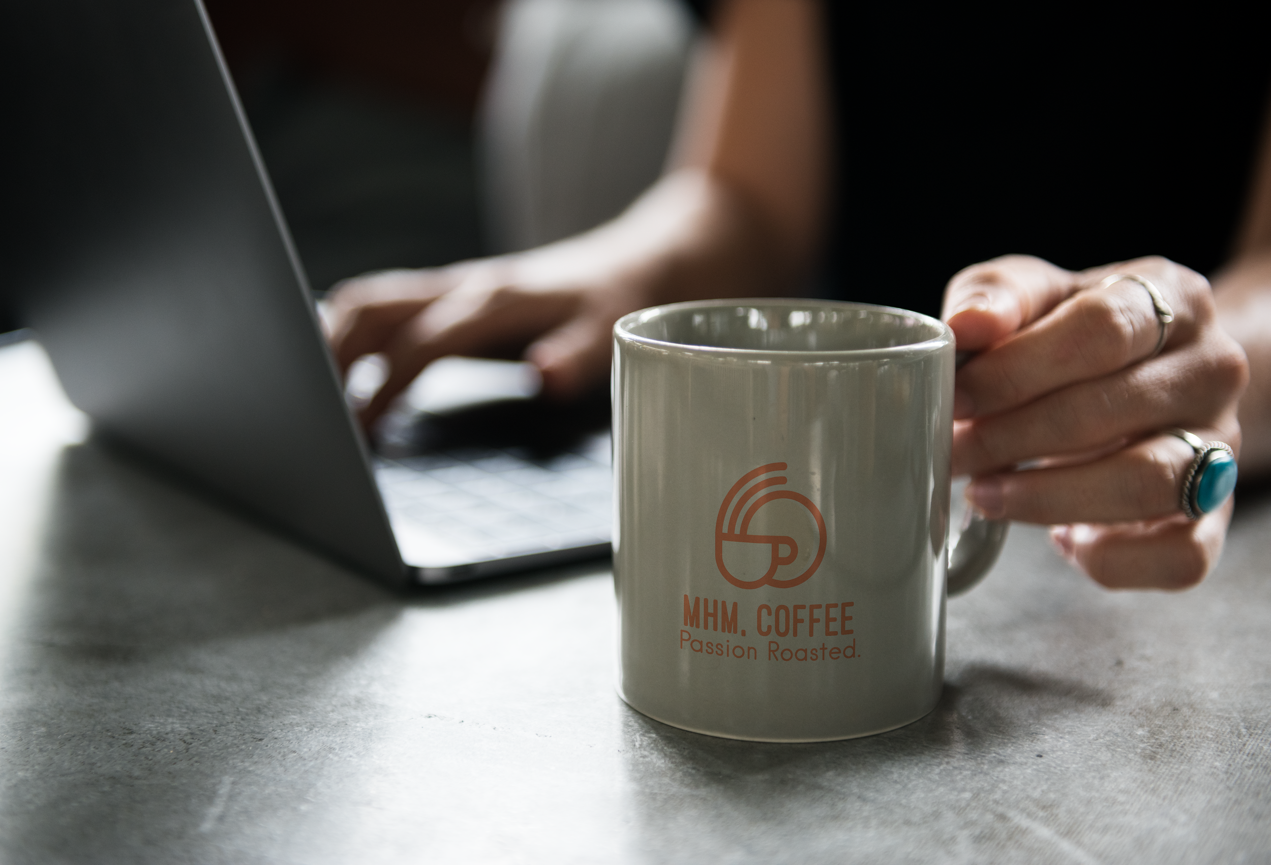 Person using a laptop with a coffee mug in the foreground on a gray surface.