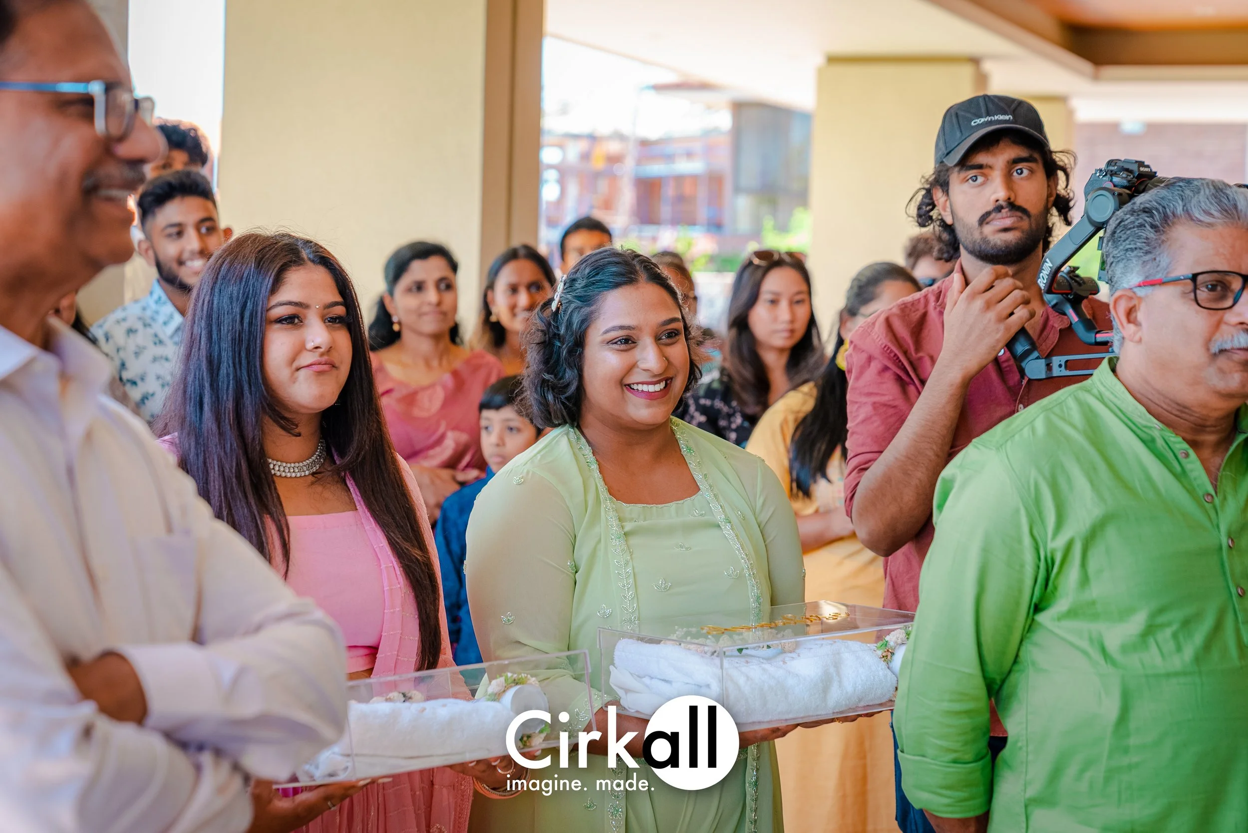 Group of people participating in a cultural or religious ceremony, holding trays with offerings or sacred items, indoors with bright natural light.