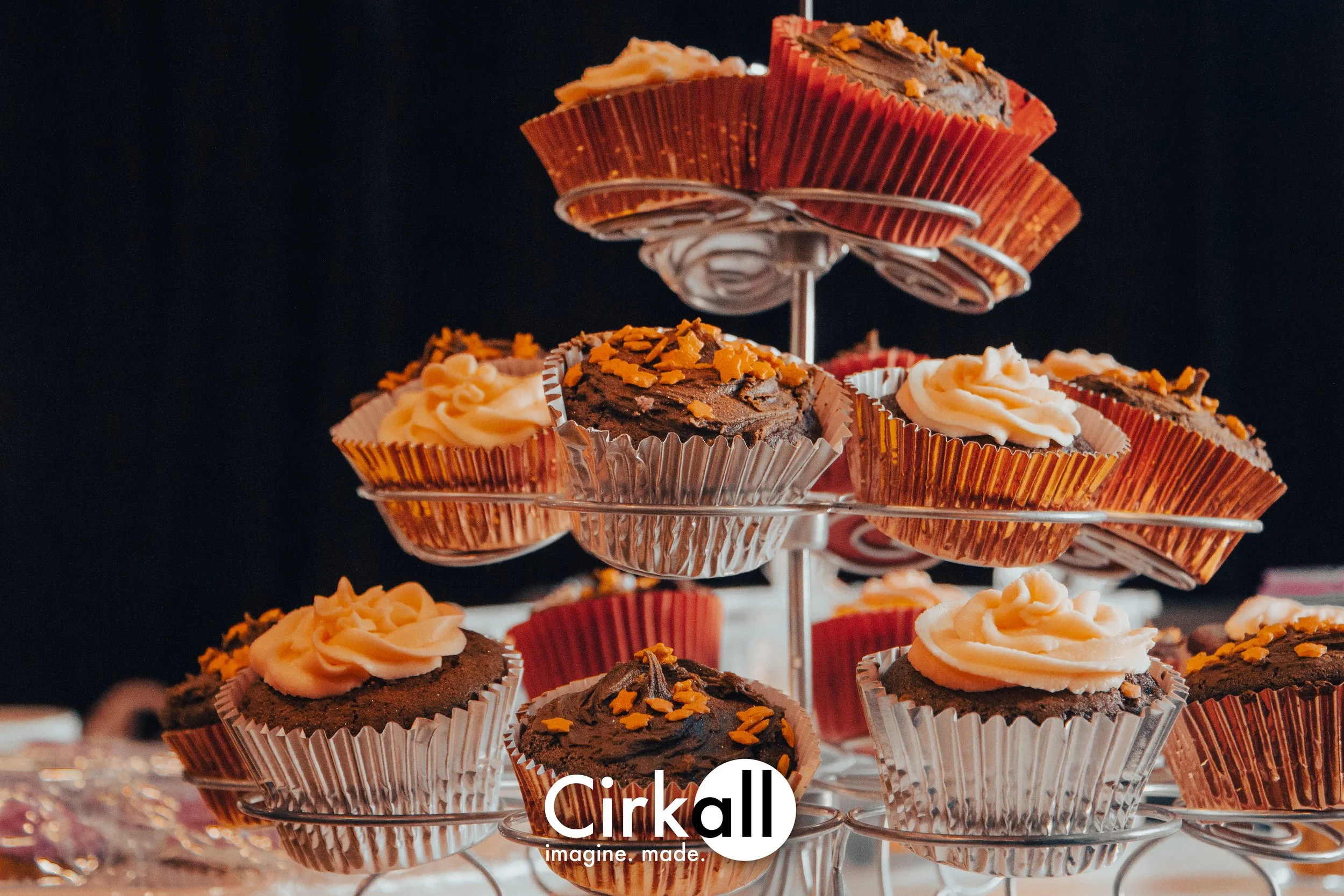 Cupcakes with vanilla and chocolate frosting on a tiered metal stand against a dark background.