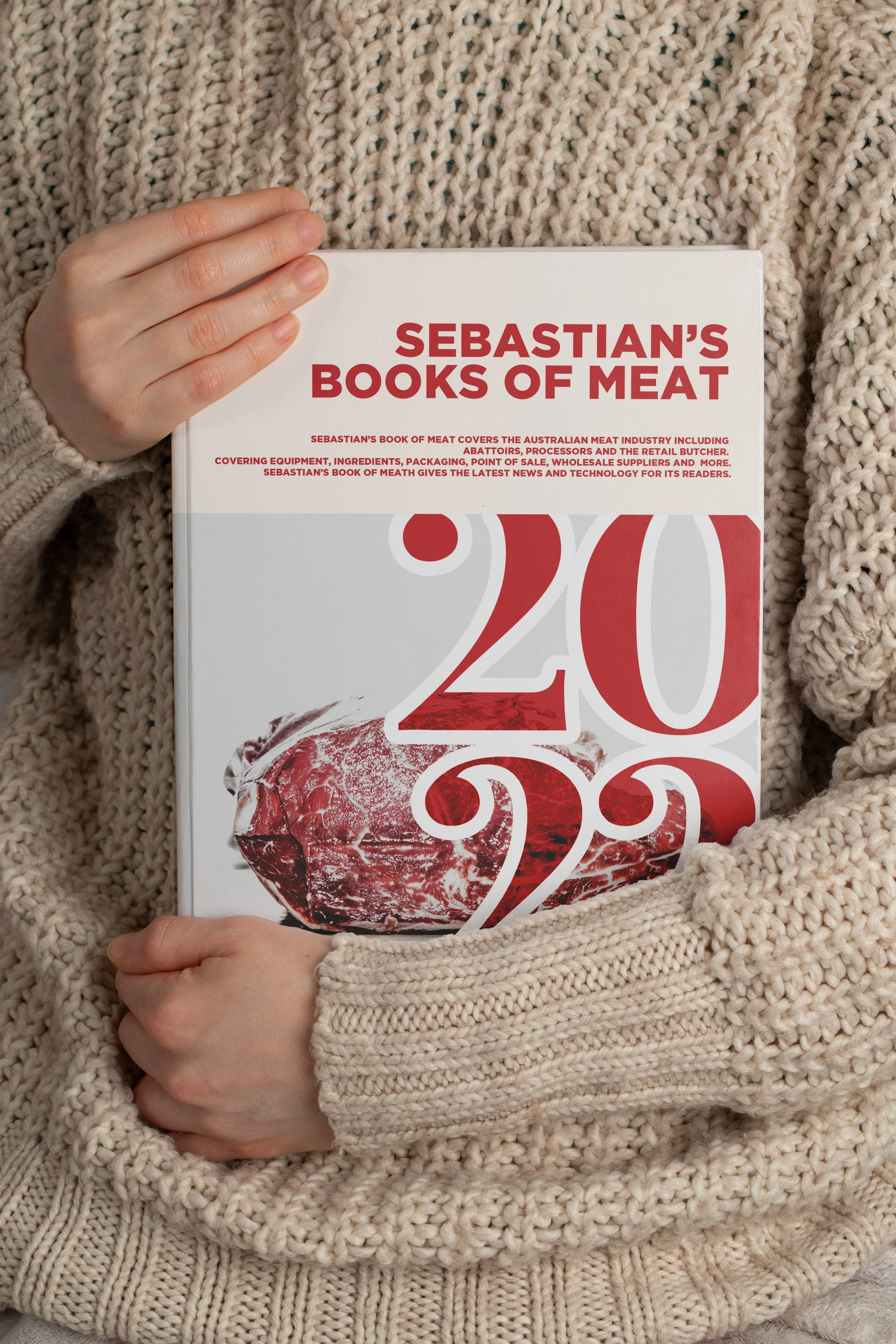 Person wearing a chunky beige knit sweater holding a book titled 'Sebastian's Books of Meat'. The cover features a large red number 20 with an image of raw meat integrated into the design.