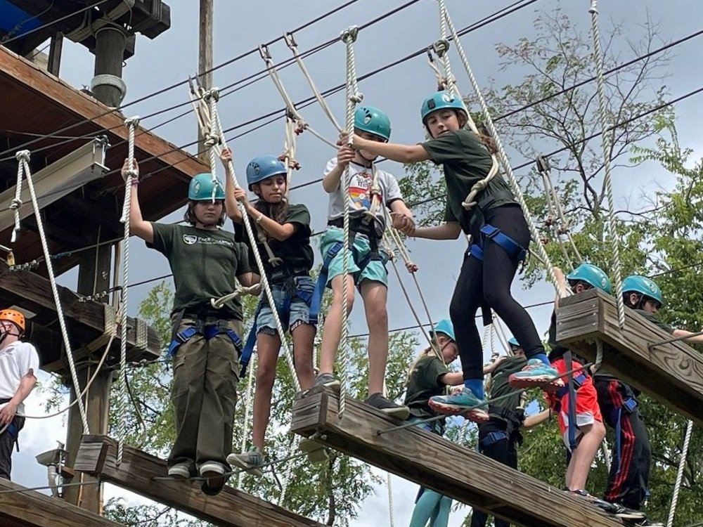 Learners in helmets and harnesses on an outdoor ropes course