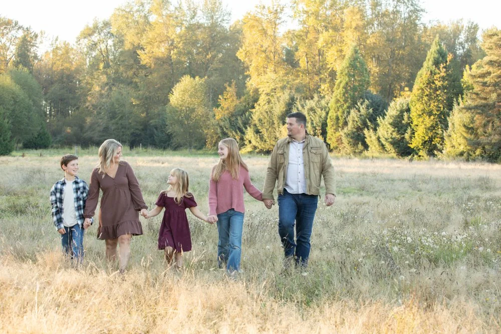 Family holding hands in a grassy field with trees in the back ground