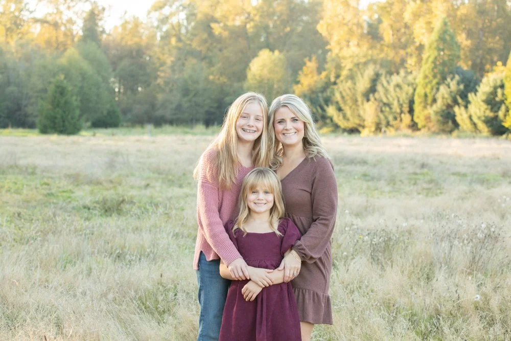 mom and two daughters standing in a field with a gorgeous tree line