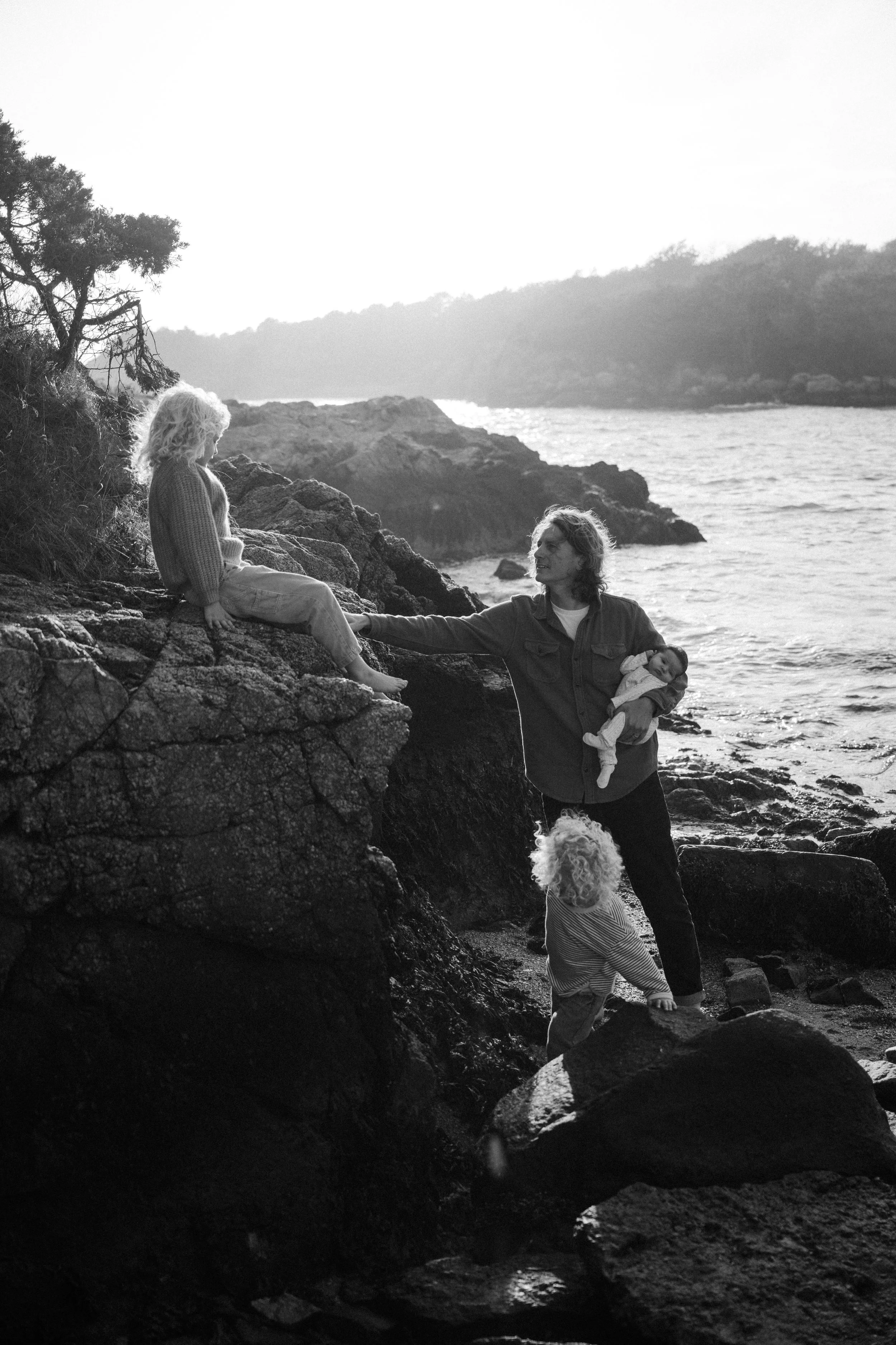 A black and white photo of a woman embracing a young girl, both with their eyes closed, sharing a tender moment outdoors. The girl is wearing a floral patterned long-sleeve shirt and the woman has long hair.