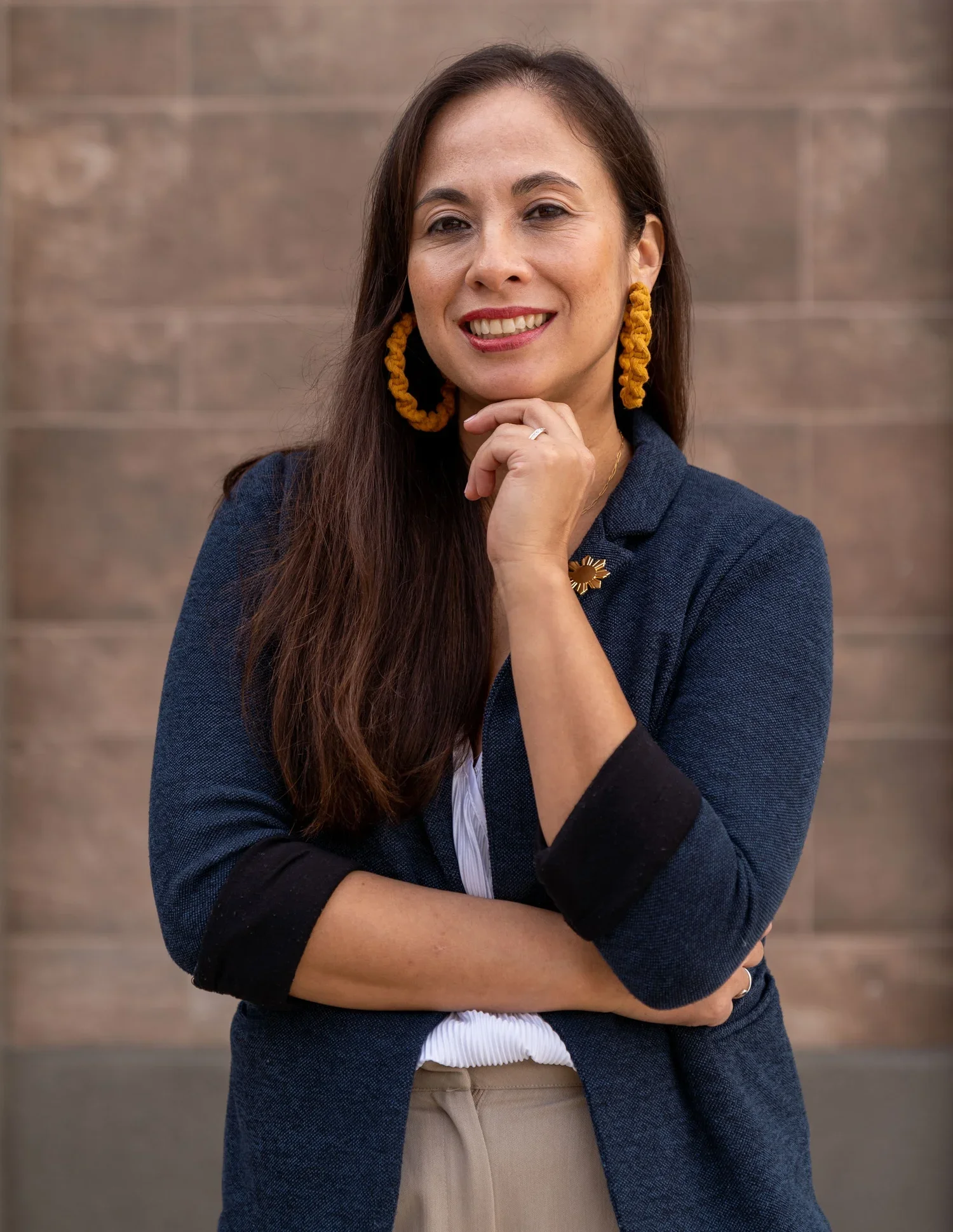 Smiling woman with straight long hair, dark jacket, and arms folded