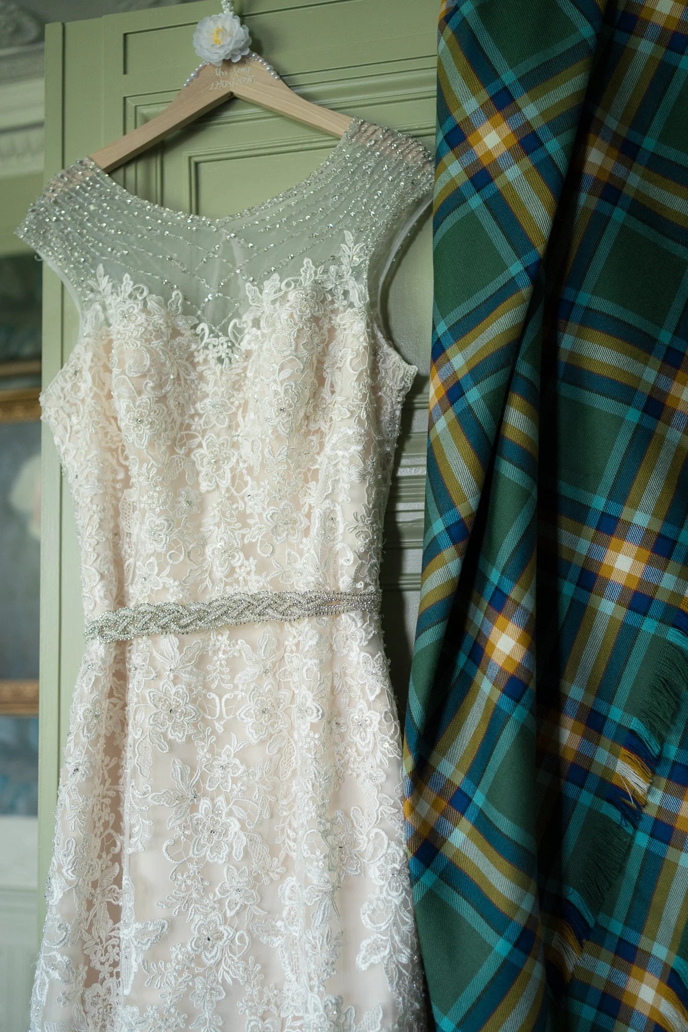 A wedding dress hanging on a hanger next to a plaid fabric.