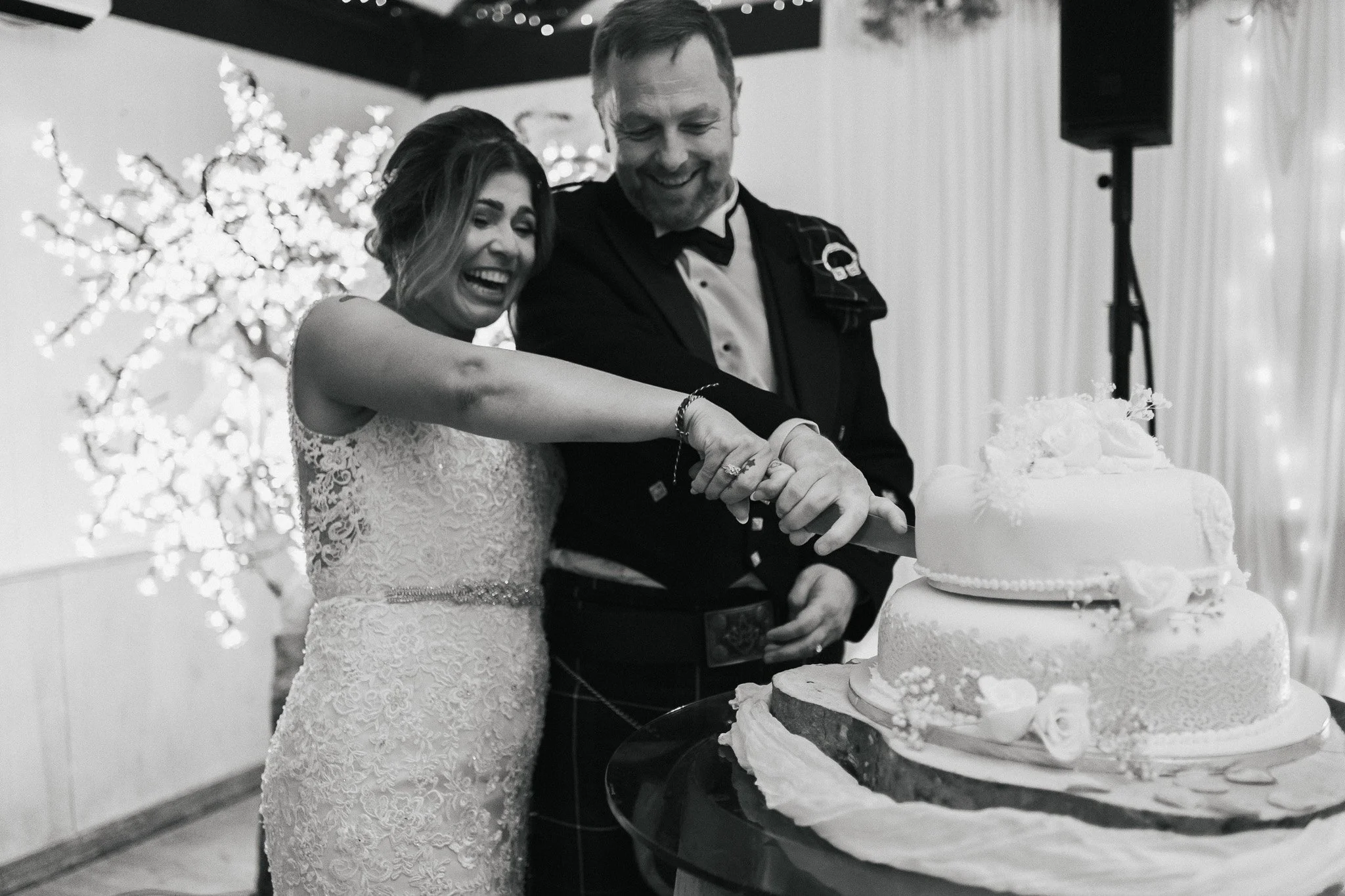 A bride and groom cutting their wedding cake at a wedding reception, smiling and sharing a joyful moment.