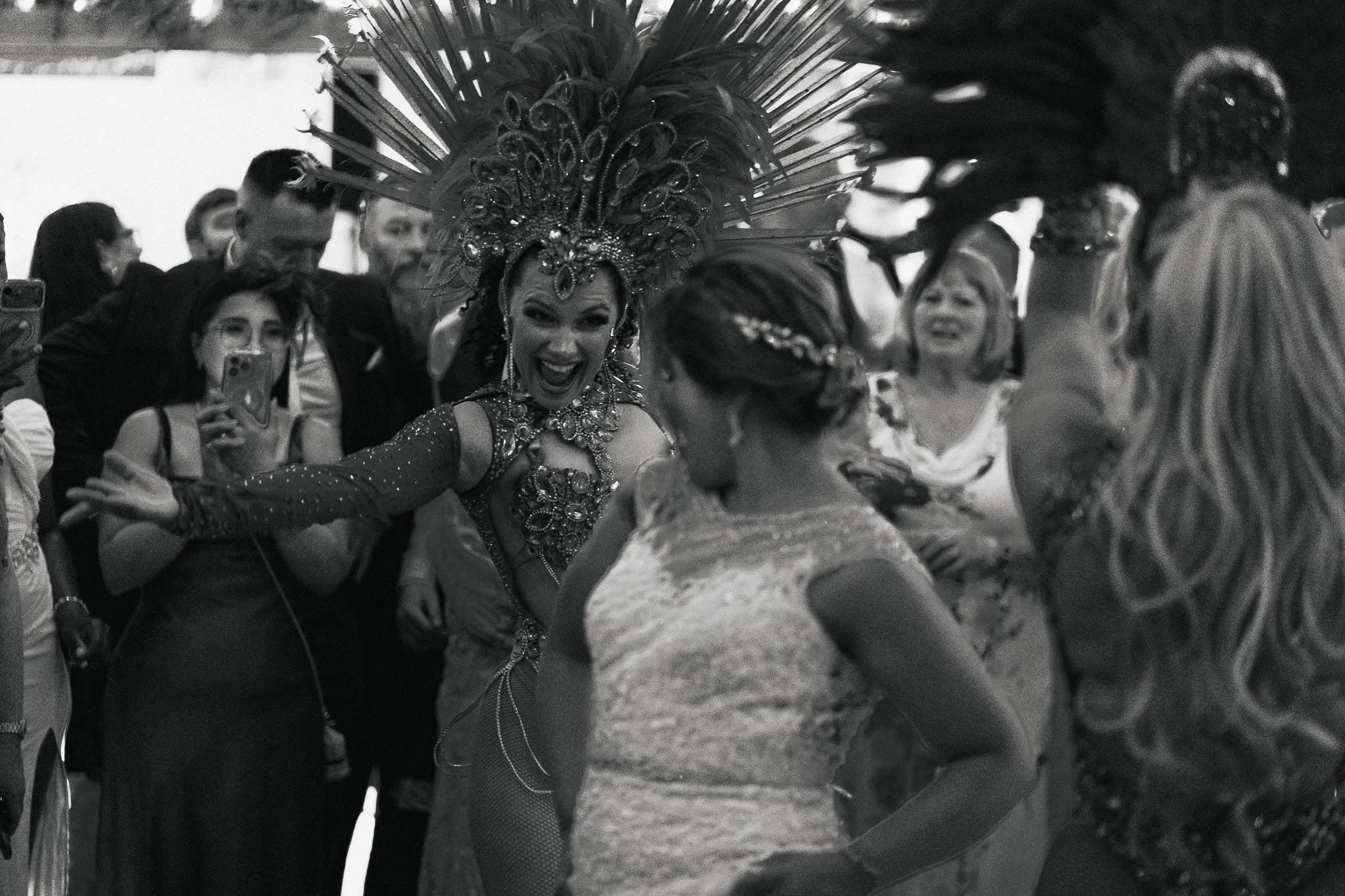 A woman in an elaborate costume with a large feathered headdress, surrounded by a group of people taking photos and smiling.