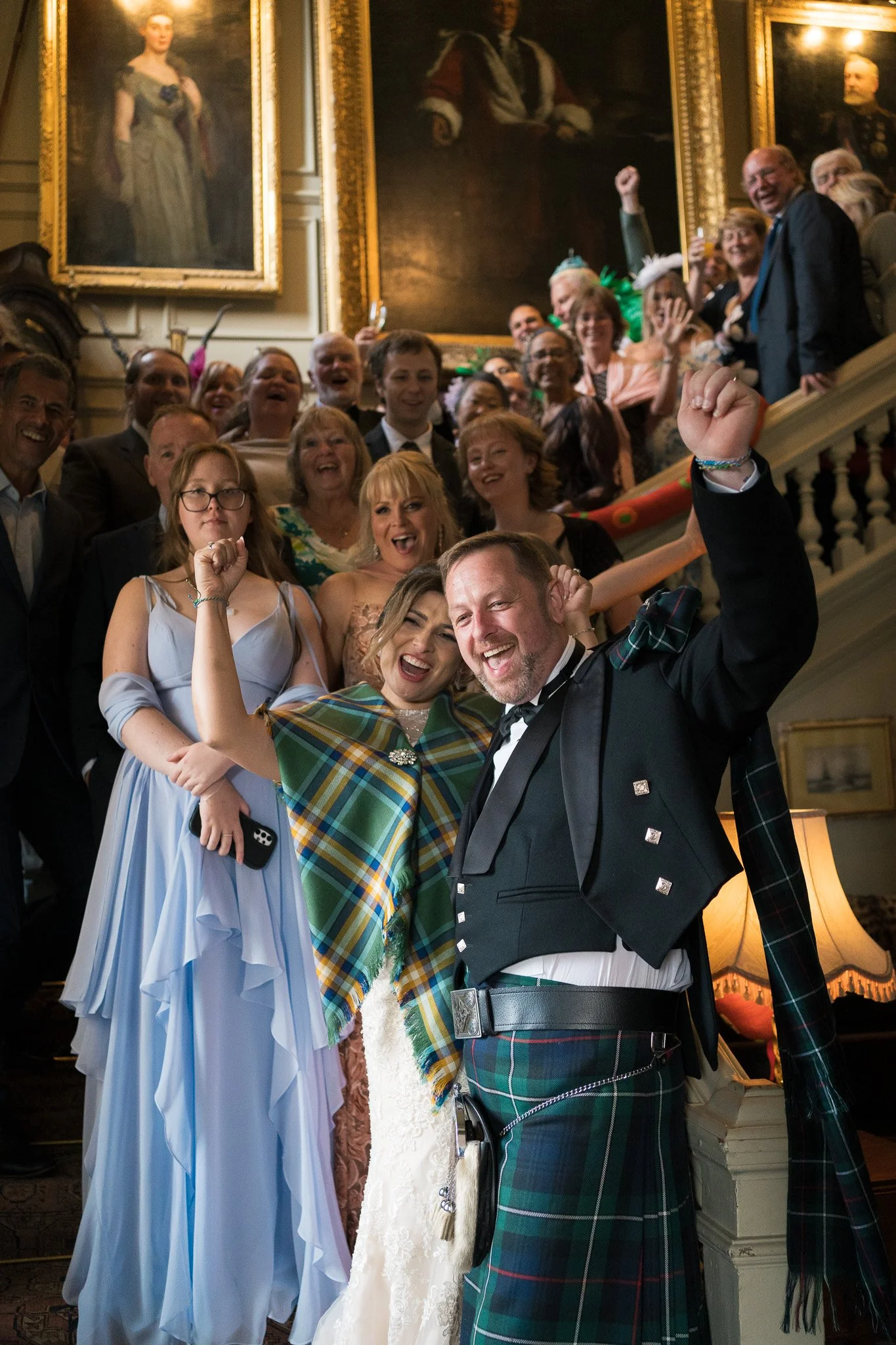 A group of people gathered on a staircase, celebrating at a fancy event, with large paintings hanging on the wall behind them.