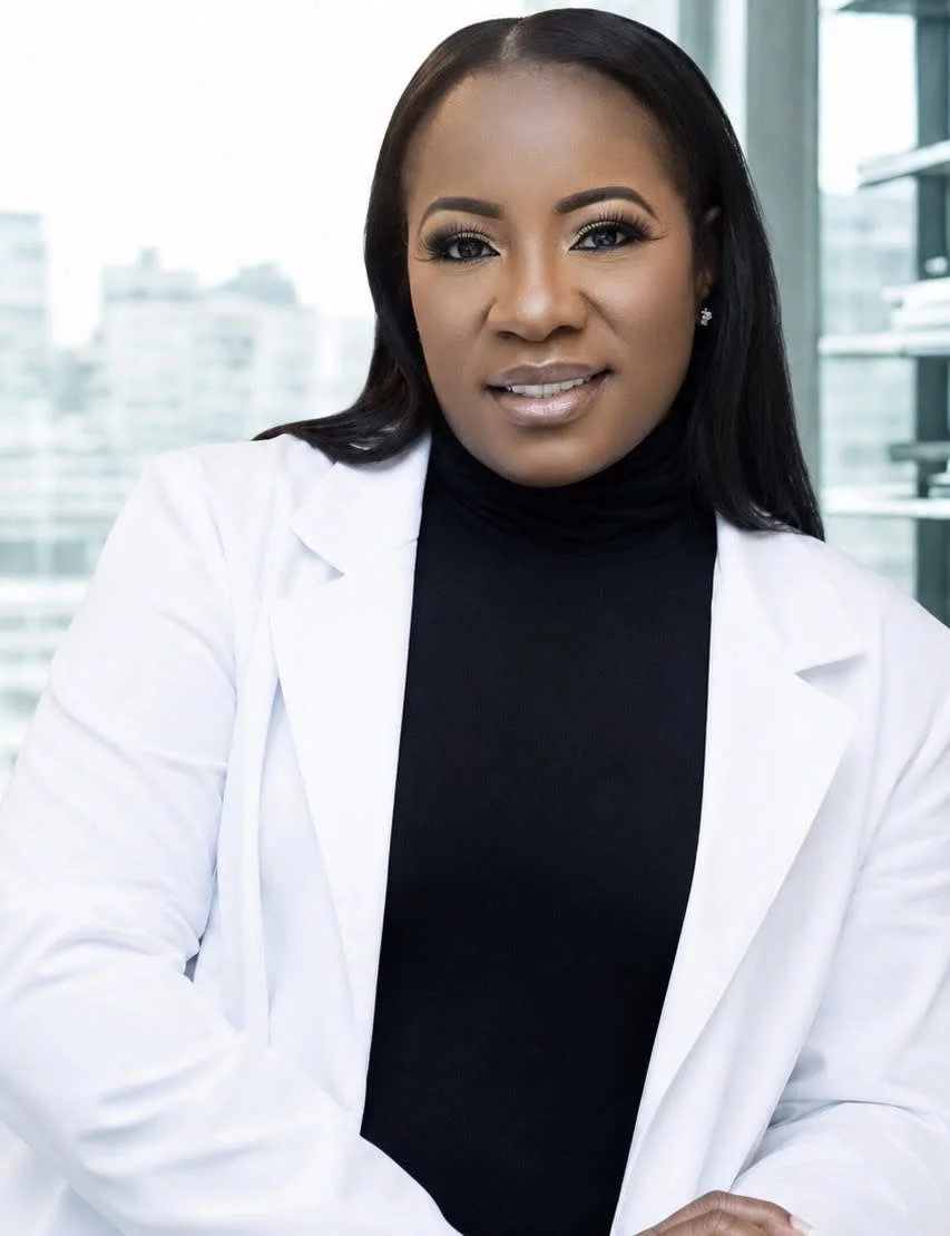 A confident African American female scientist or doctor with long black hair, wearing a white lab coat and a black turtleneck, in a modern office or laboratory with large windows and cityscape view.