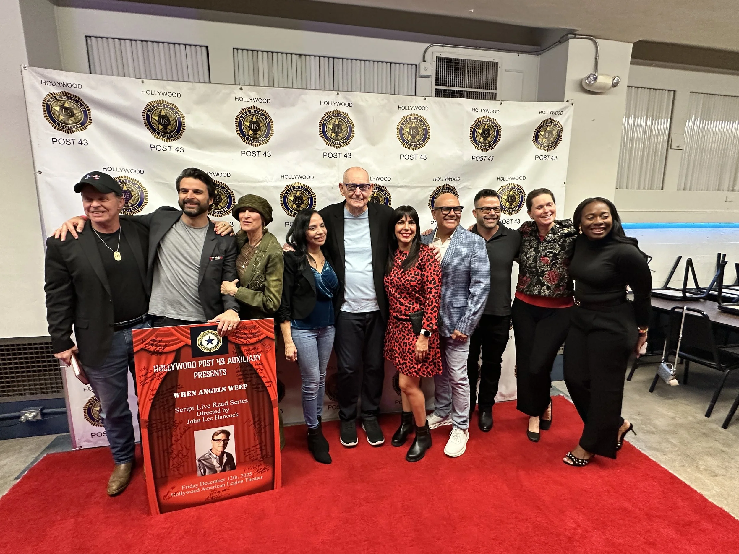 A group of eleven people standing together on a red carpet in front of a backdrop with the Hollywood POST 43 emblem. They are smiling and posing for a photo at an event, with a poster in front announcing a live read series titled 'When Angels Weep' directed by John Lee Hancock.