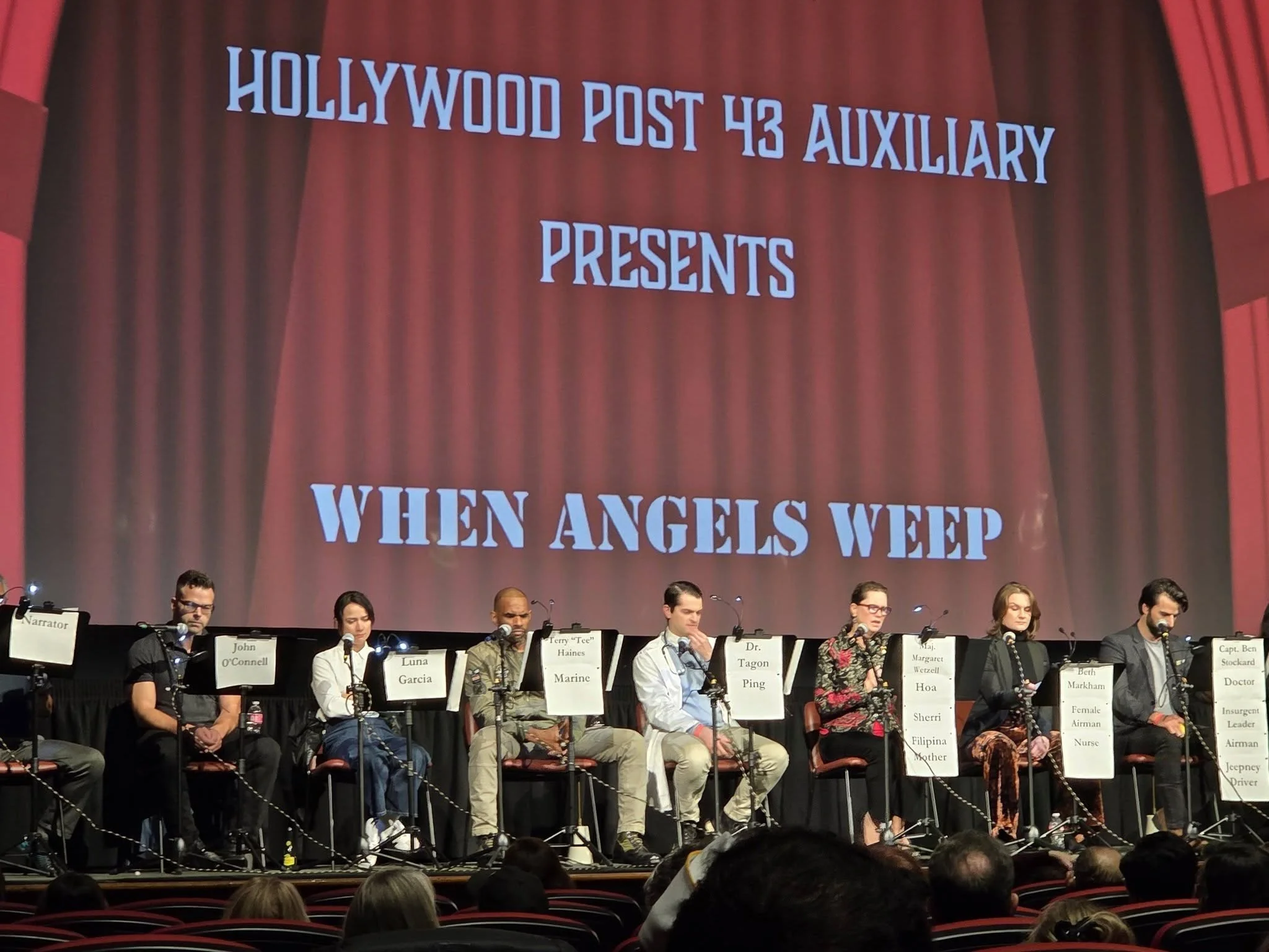 Panel of speakers sitting on stage with large red curtain backdrop. Display reads 'Hollywood Post 43 Auxiliary Presents When Angels Weep.'