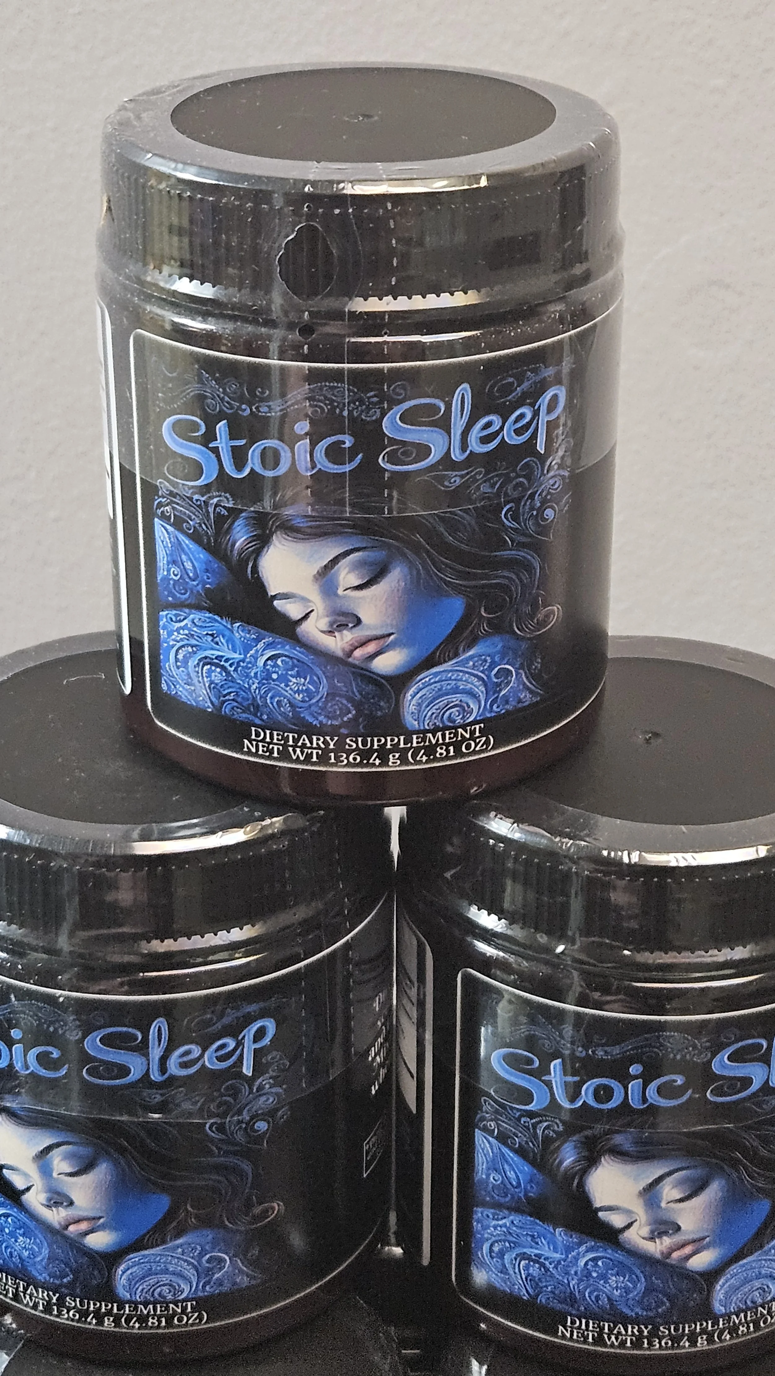 Three black bottles of dietary supplement named 'Stoic Sleep' with an illustration of a woman peacefully sleeping on the label.