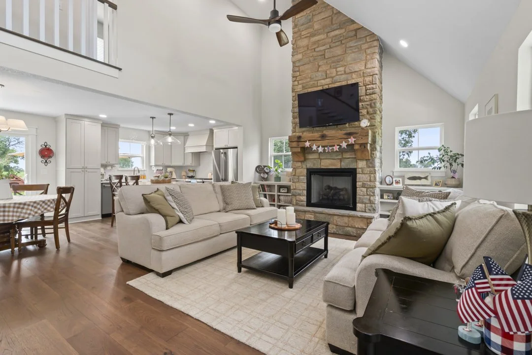 Open-concept living room with vaulted ceilings, stone fireplace, and seamless flow into the kitchen and dining areas.