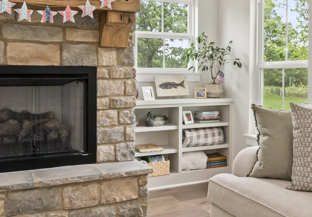 Stone fireplace with custom built-in shelving and large windows creating a warm and inviting living space in a custom home.