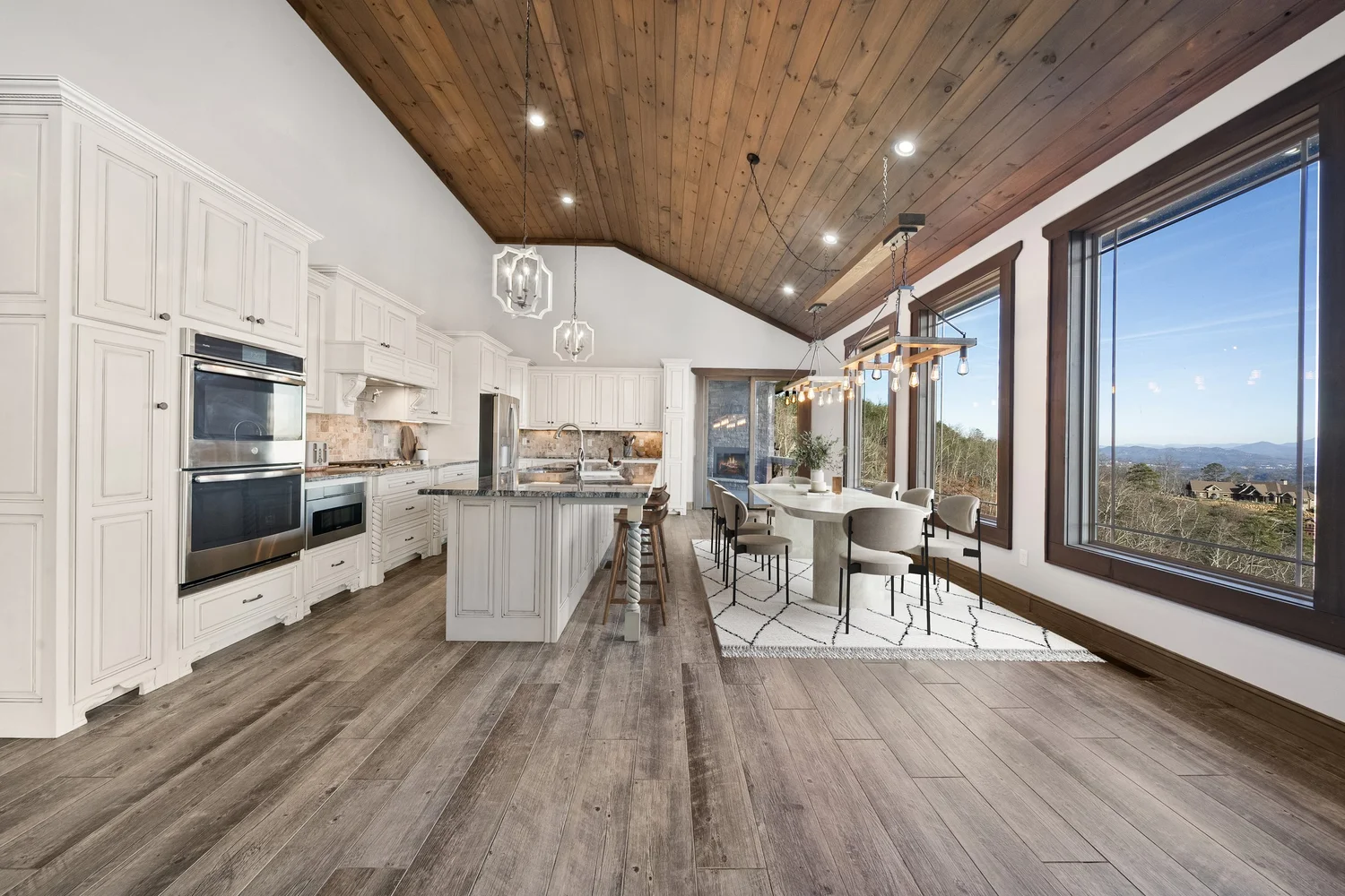 A bright white kitchen with a wood ceiling, oversized island and expansive windows.