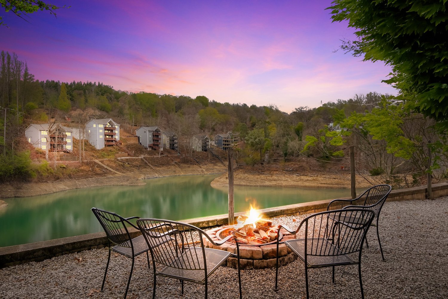 A lakeside firepit and seating area at dusk with a colorful sky reflected in the water.