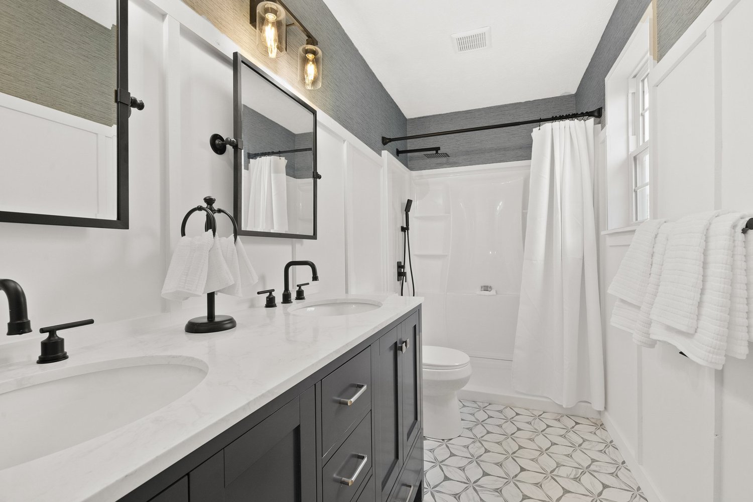 A modern bathroom with dark cabinetry, white tile and black fixtures.