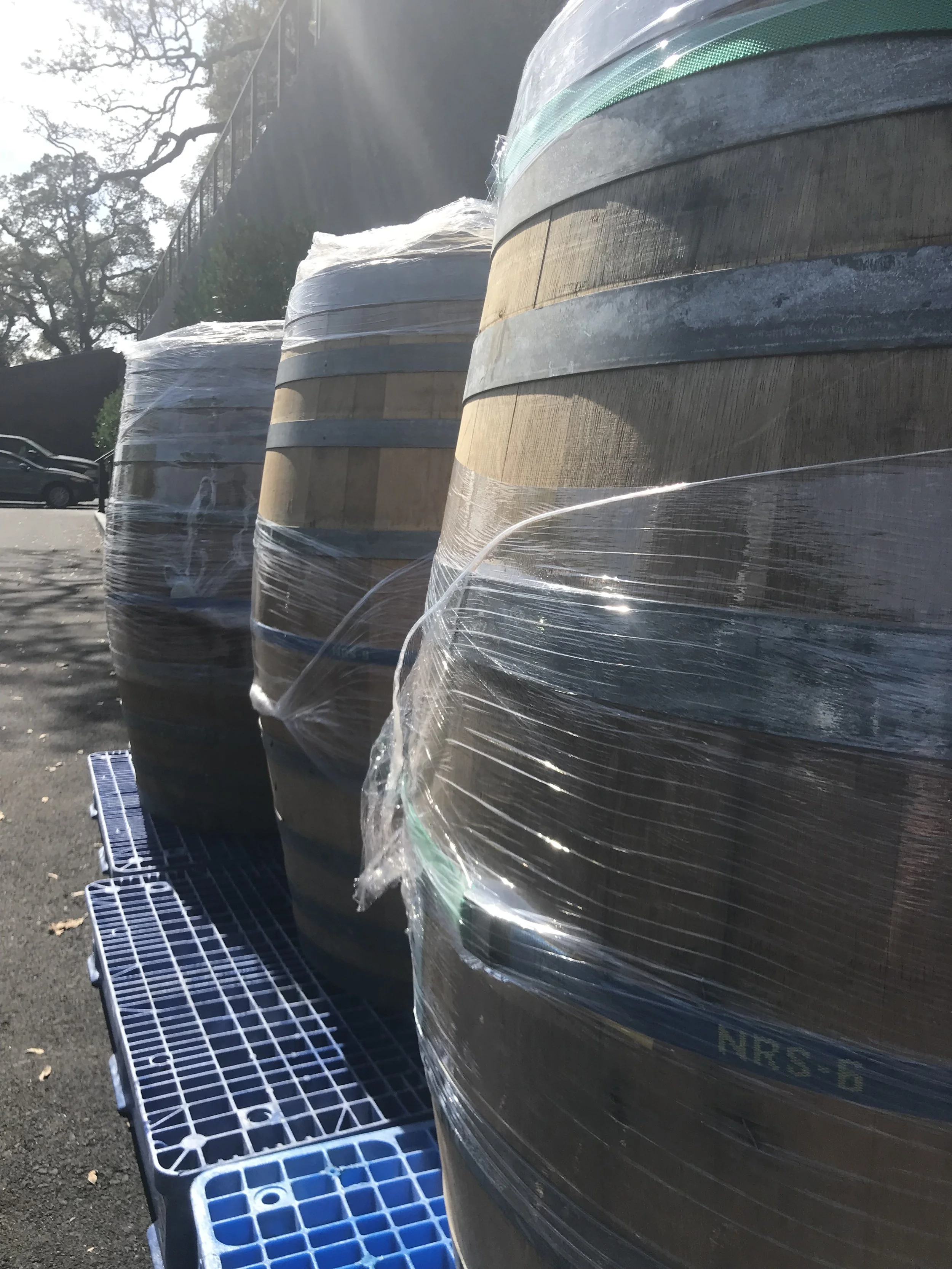 Large wooden spools wrapped in plastic on a blue pallet in an outdoor parking lot.