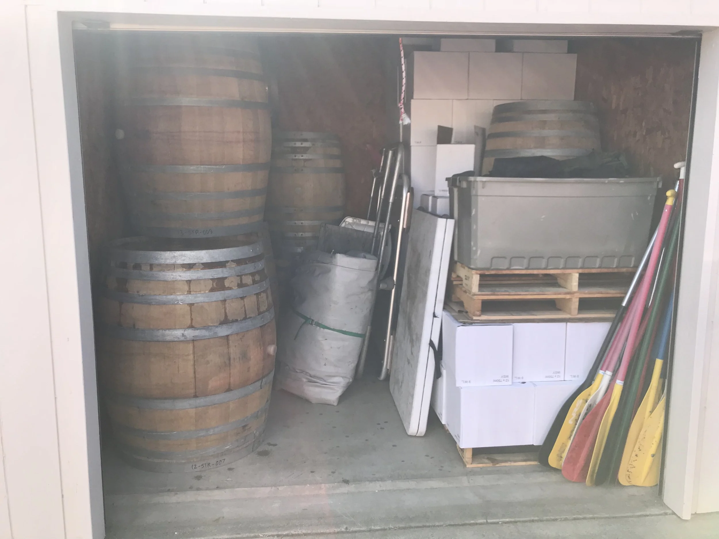 Storage closet with wooden barrels, cardboard boxes, and paddles.