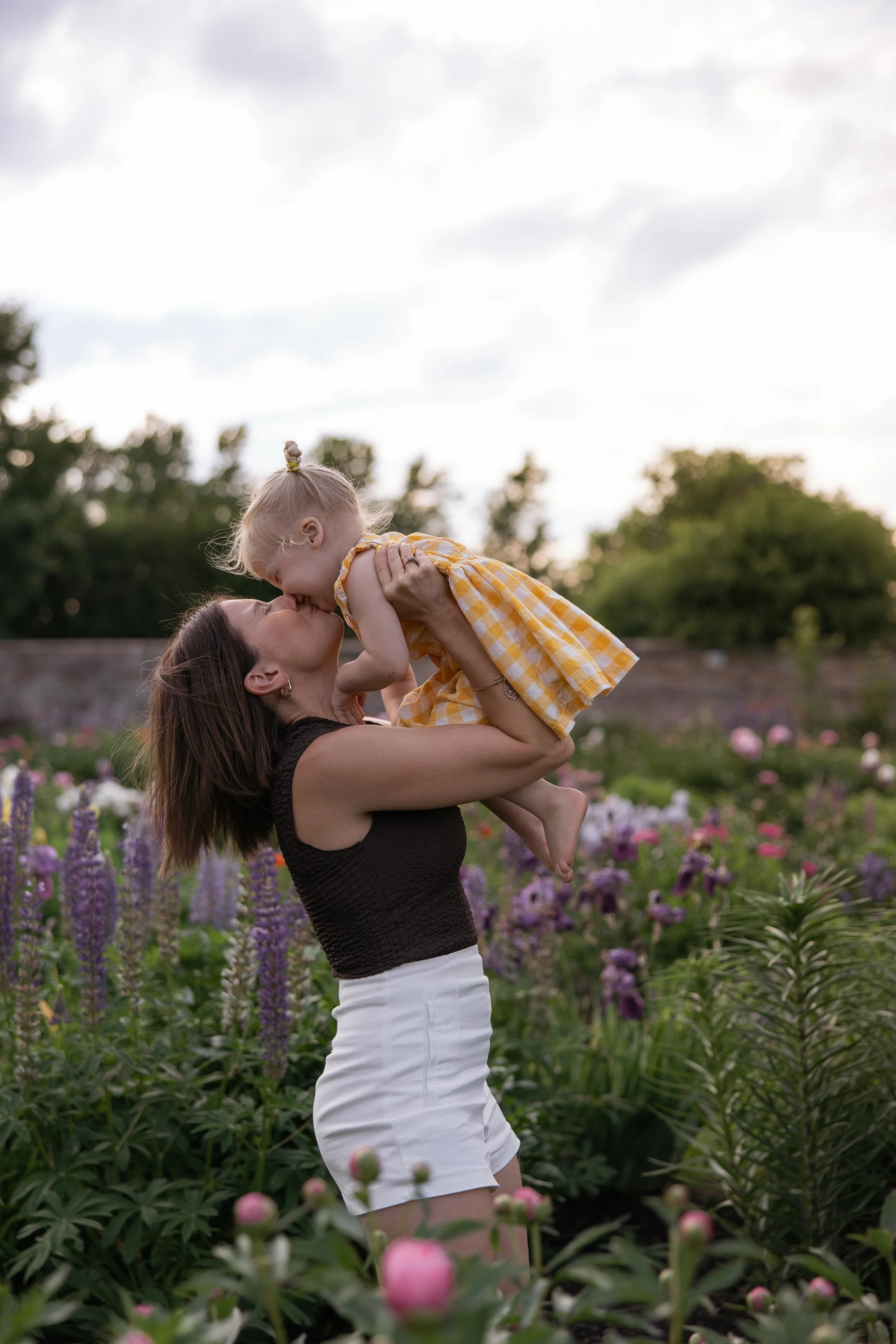 A mother in a field of wildflowers holding her kiddo up and kissing them playfully during a family photoshoot in ottawa