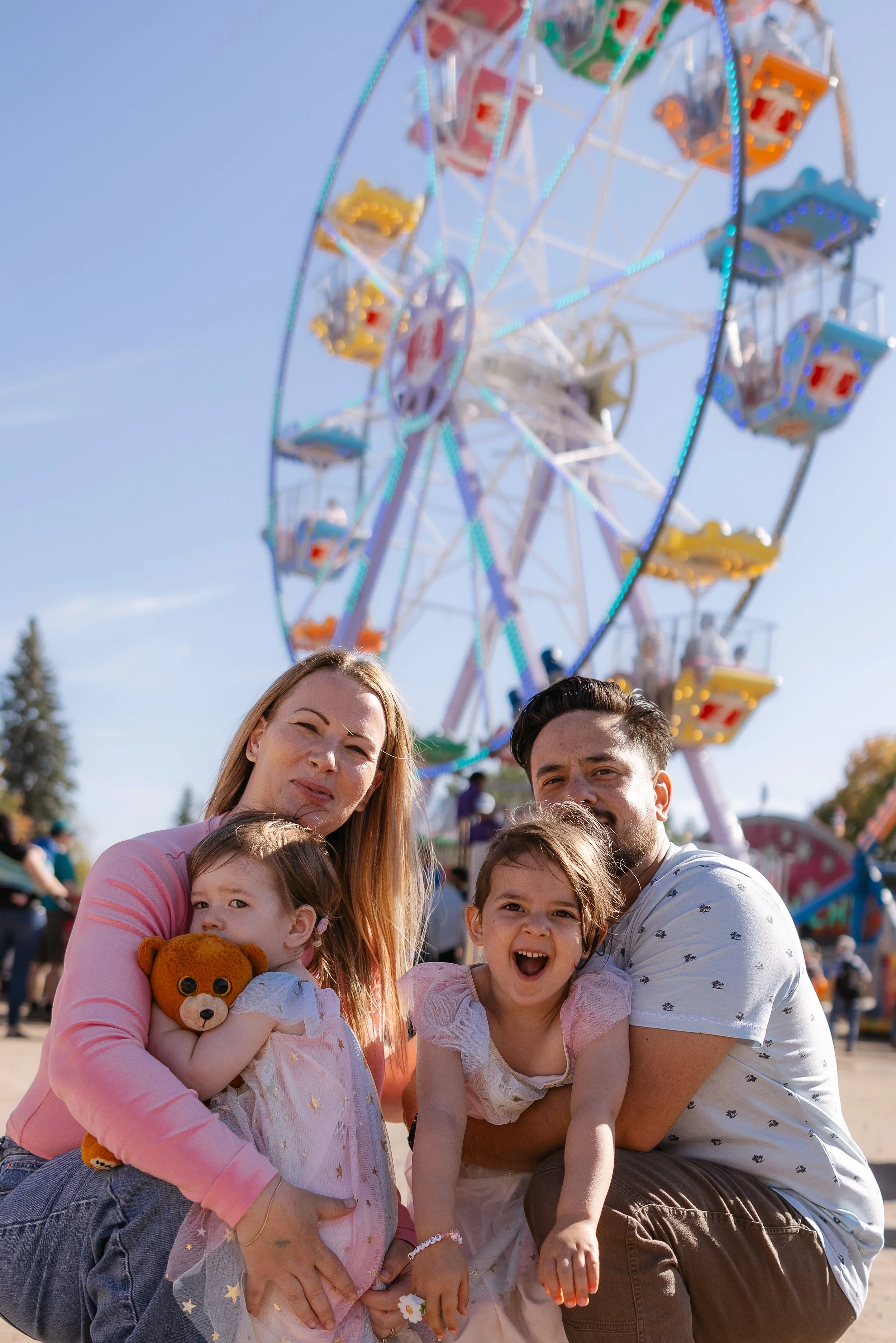 a family cuddled together in front of the ferris wheel at the carp fair for an ottawa mini session photoshoot