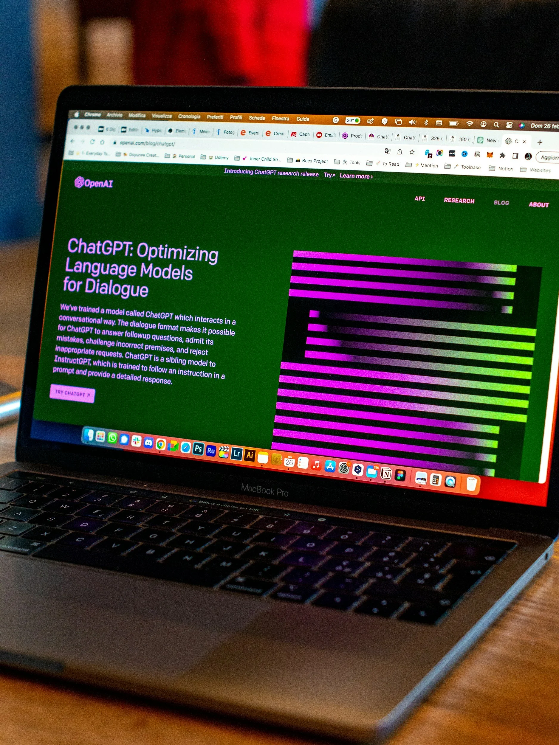 OpenAI website displayed on a MacBook Pro screen with information about optimizing language models for dialogue, featuring a graphic of pink and green horizontal lines.