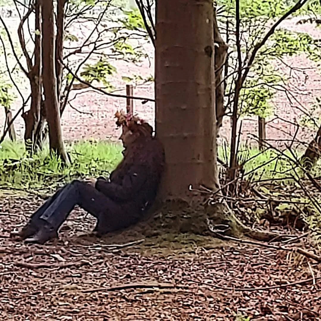 person sitting with their back against a tree in the forest