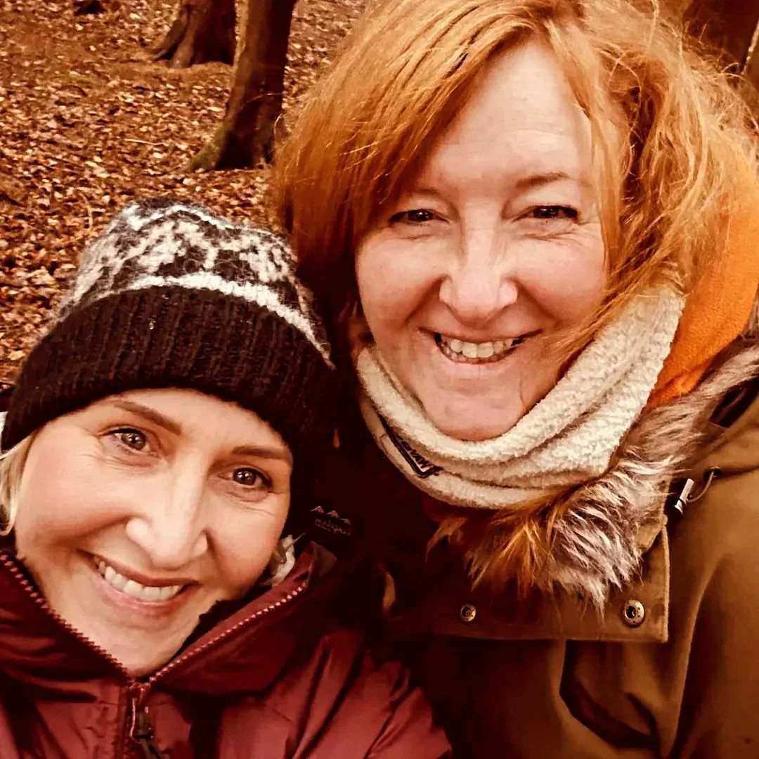 two ladies smiling with the forest floor and trees in the background